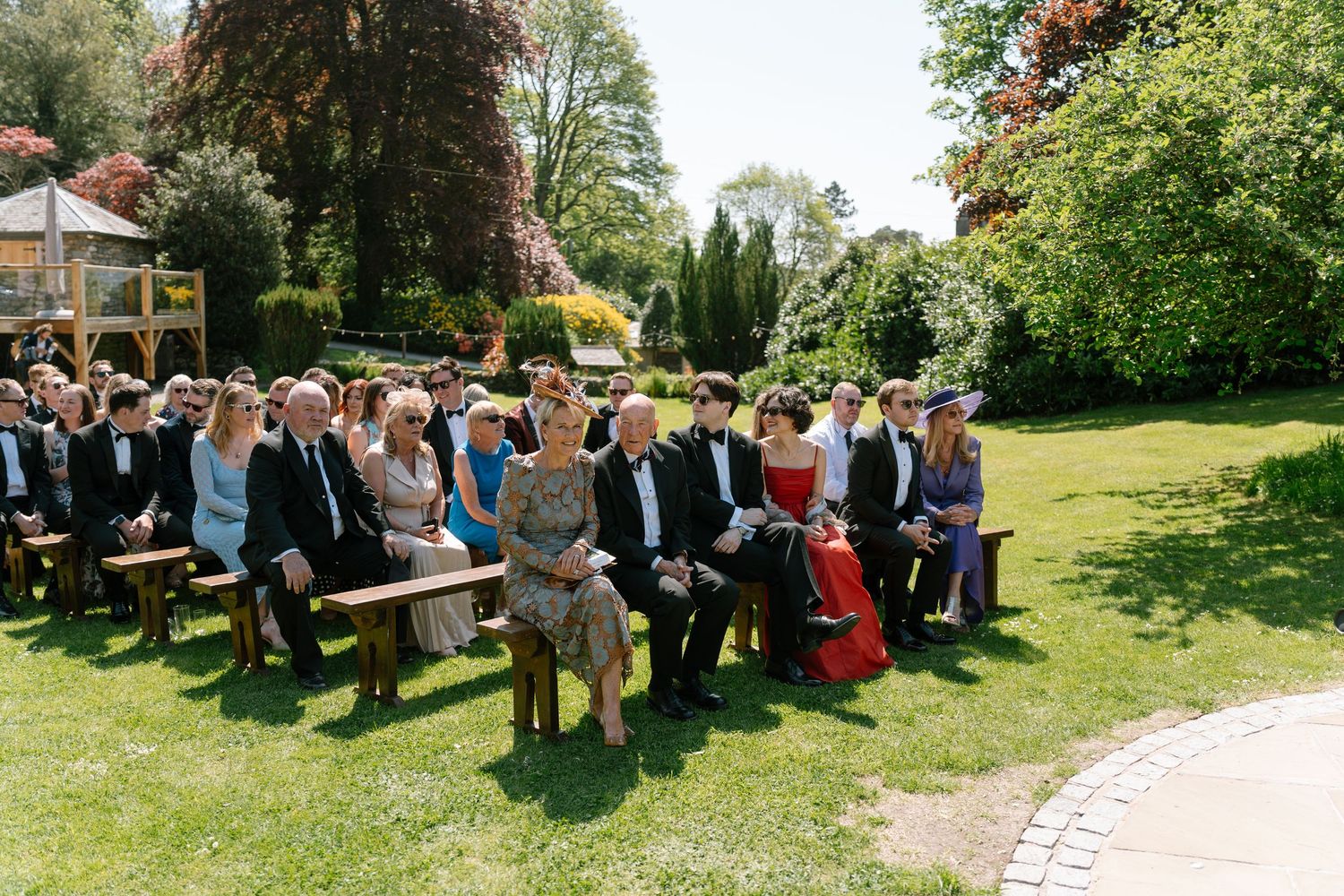 Wide angle view of wedding guests seated outdoors during a sunny ceremony.