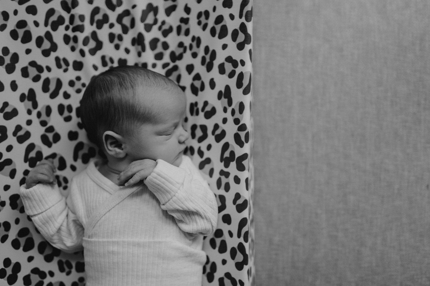 Baby resting on leopard print fabric in natural light.