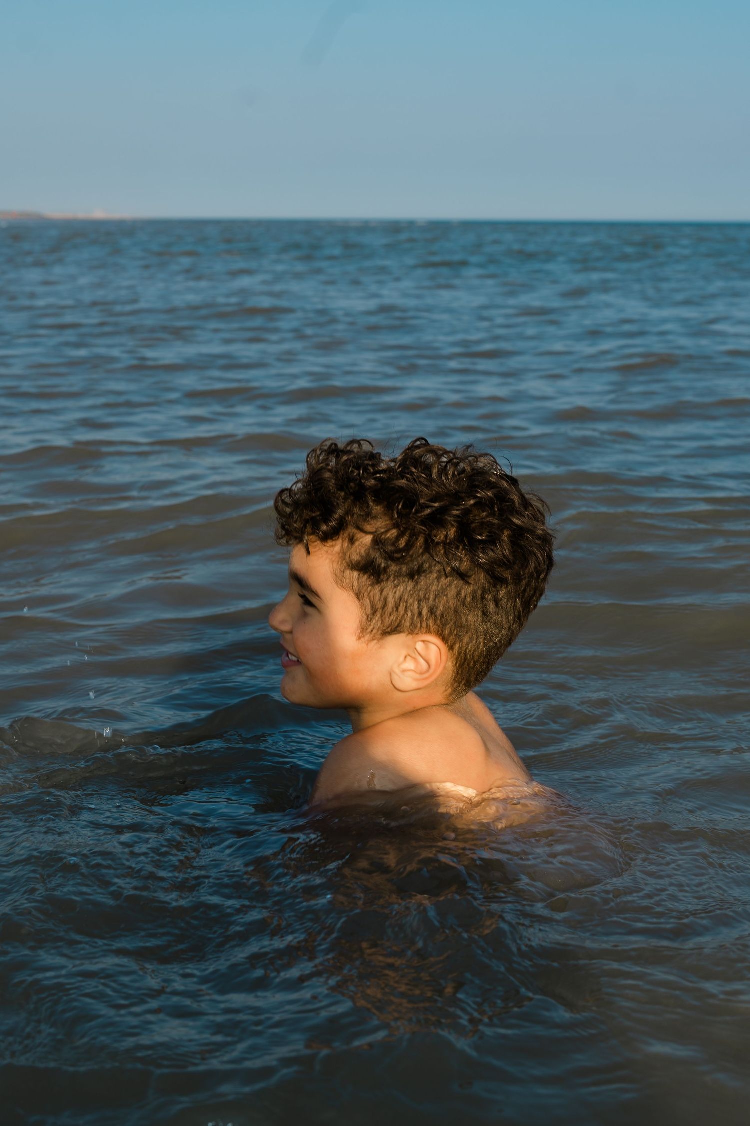 Curly-haired swimmer floating in deep blue ocean waters during summer.