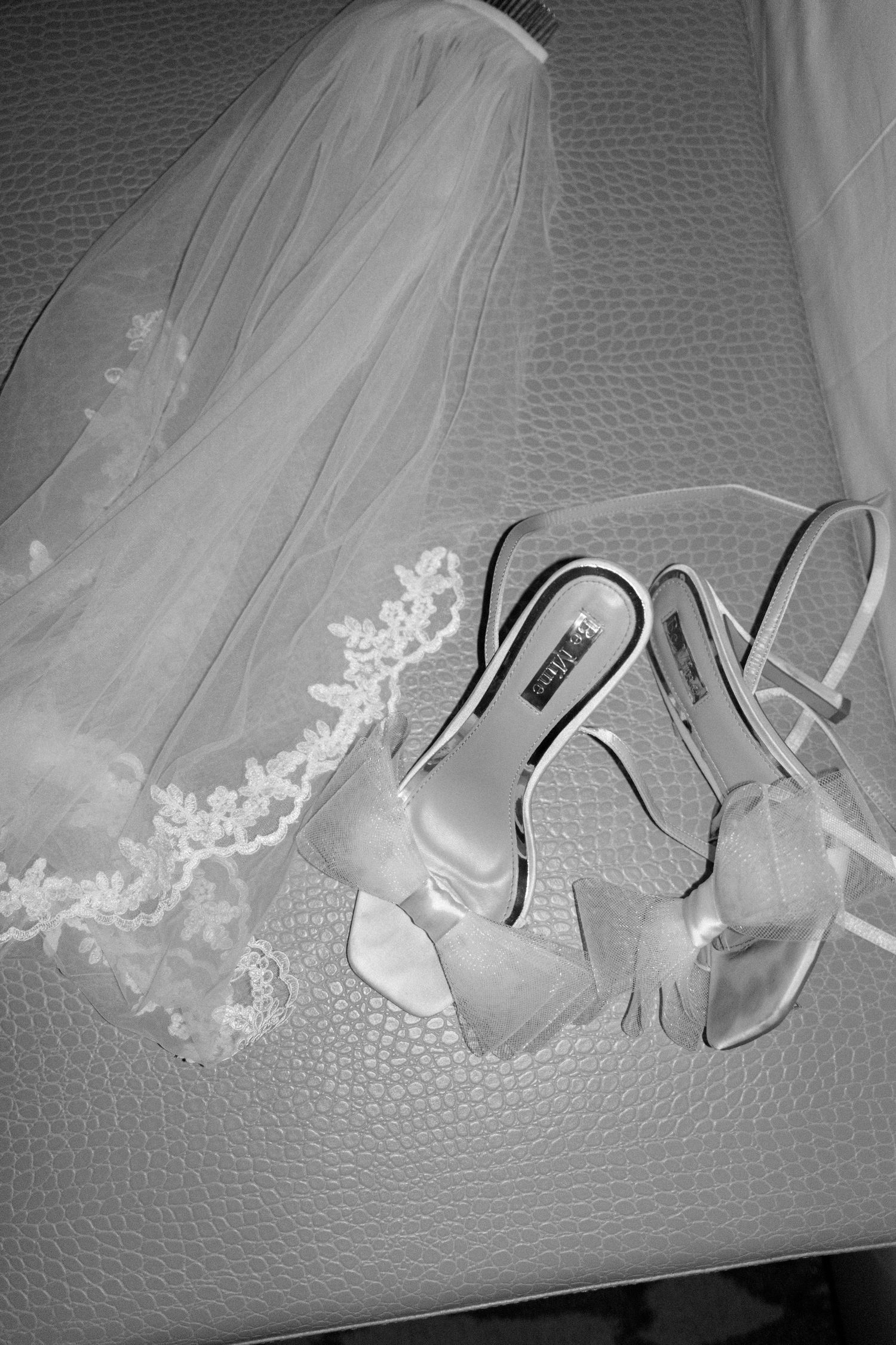 Wedding accessories including a delicate lace veil and elegant white heels arranged on a textured surface.