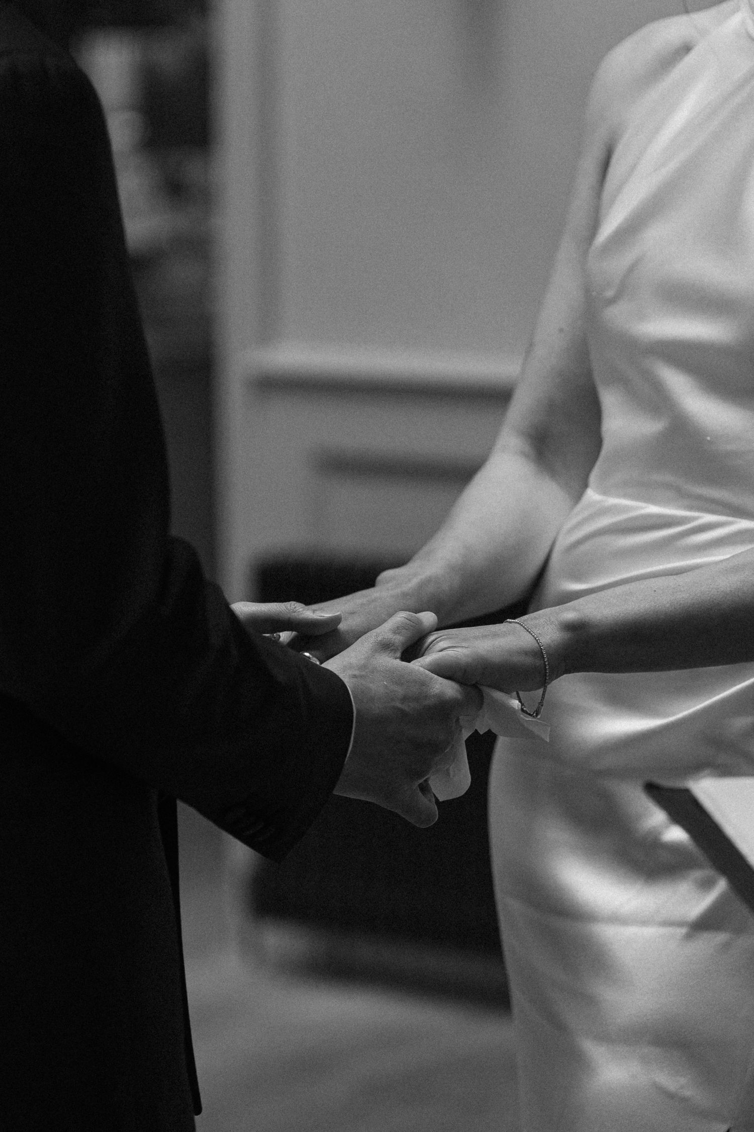 Close-up of bride and groom holding hands during their wedding ceremony in black and white.