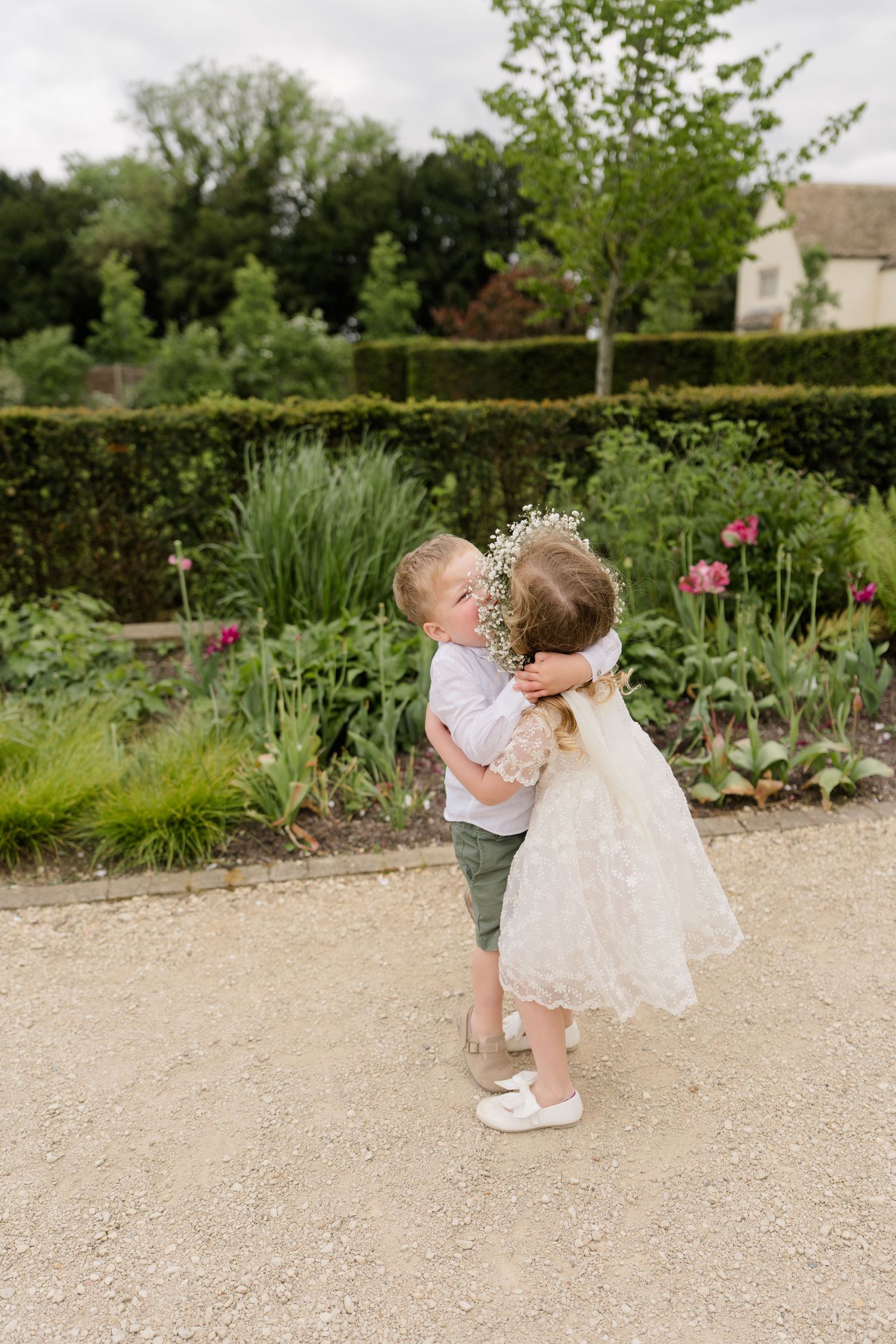 Adorable flower girl and page boy share a sweet hug in a lush garden during a wedding celebration.