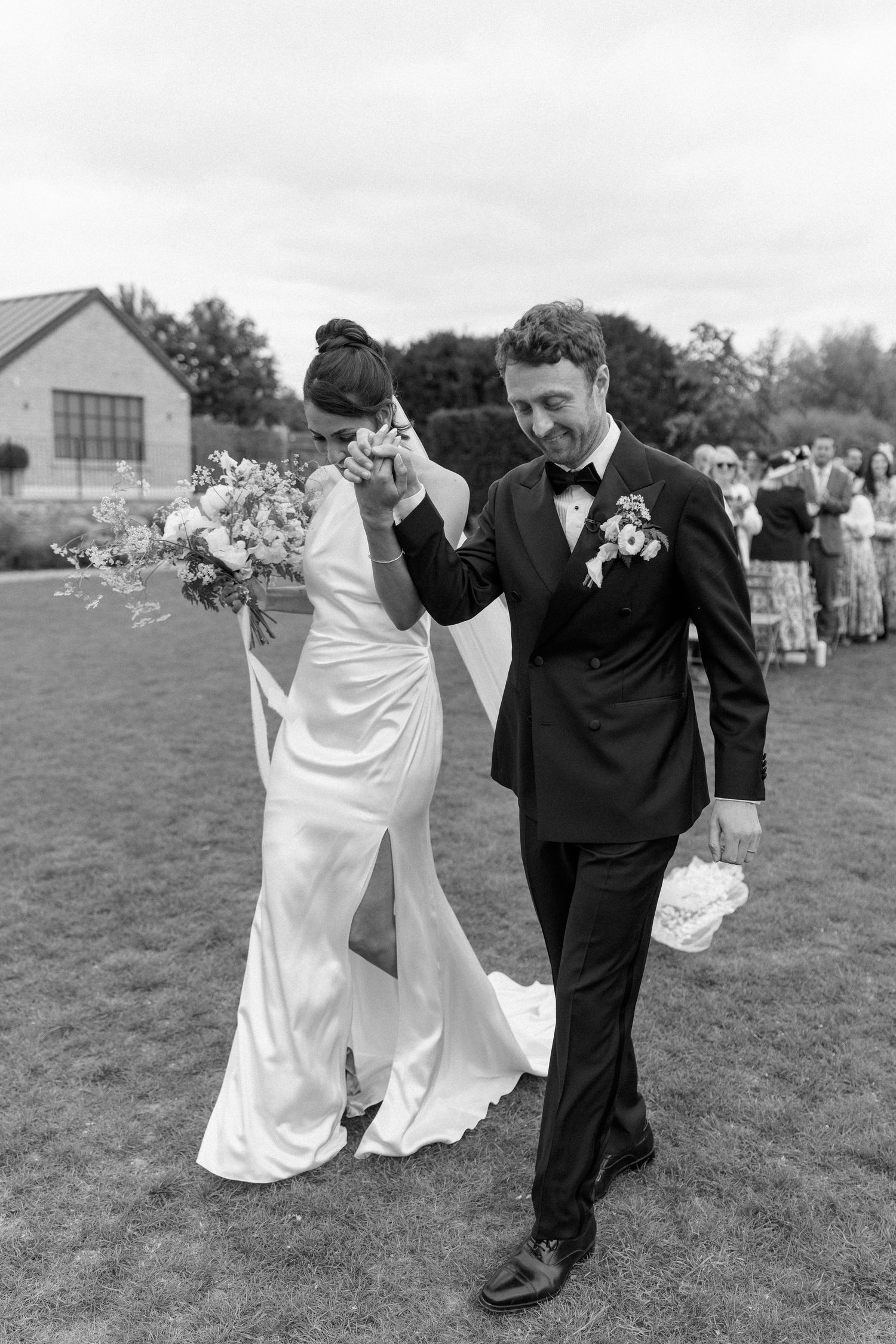 Emotional bride and groom walking away after outdoor wedding ceremony in black and white.