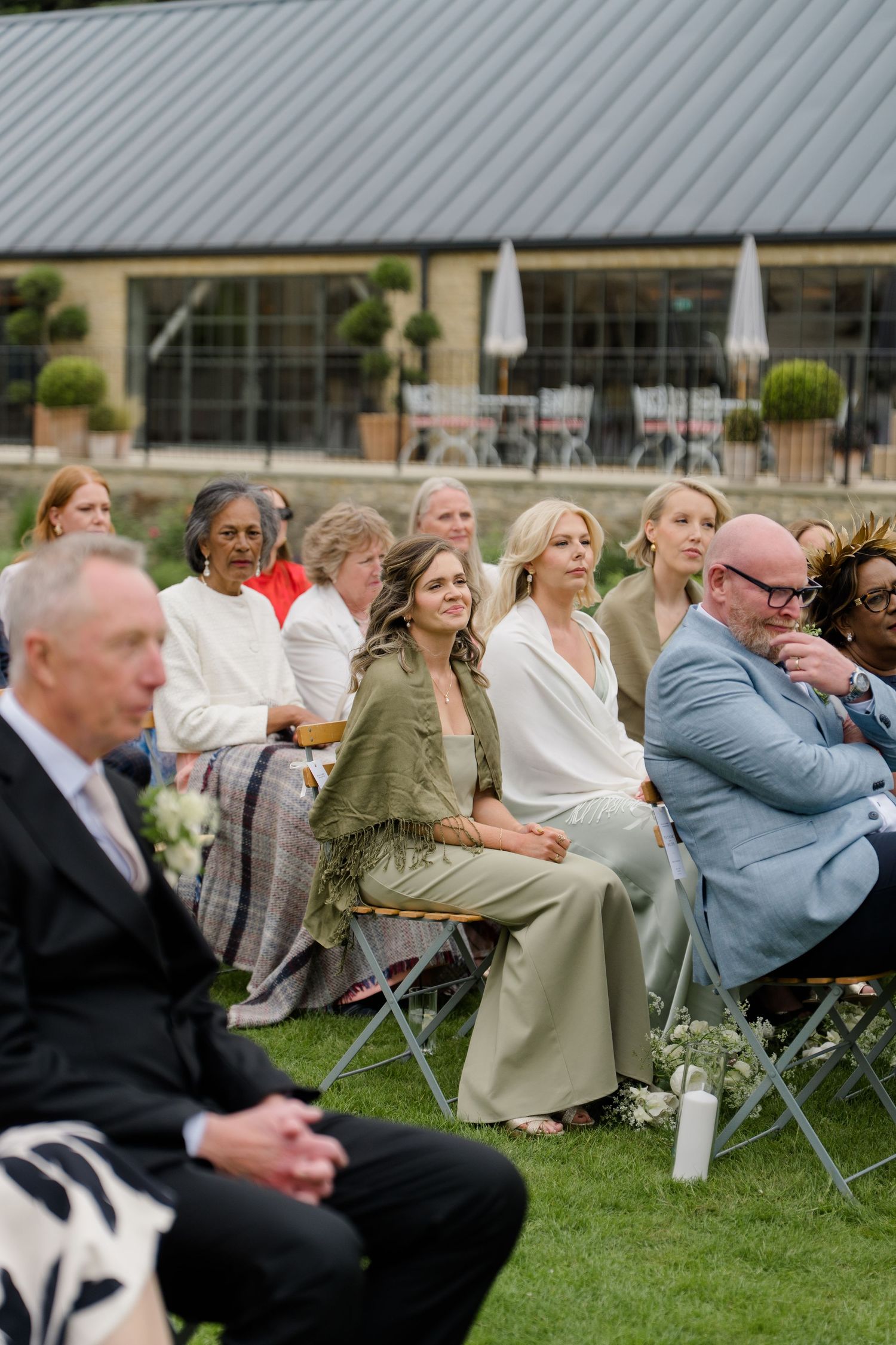 Wedding guests seated outdoors on lawn watching ceremony at elegant countryside venue.