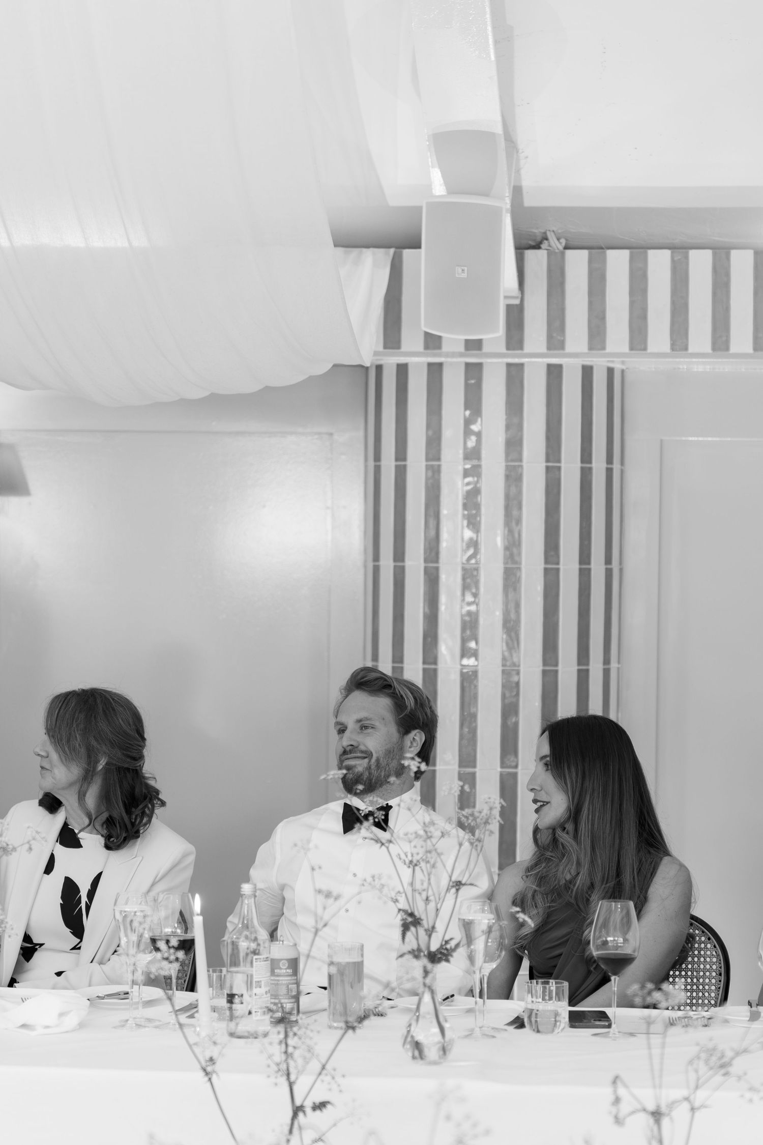 Smiling wedding guests seated at reception table inside striped marquee venue.