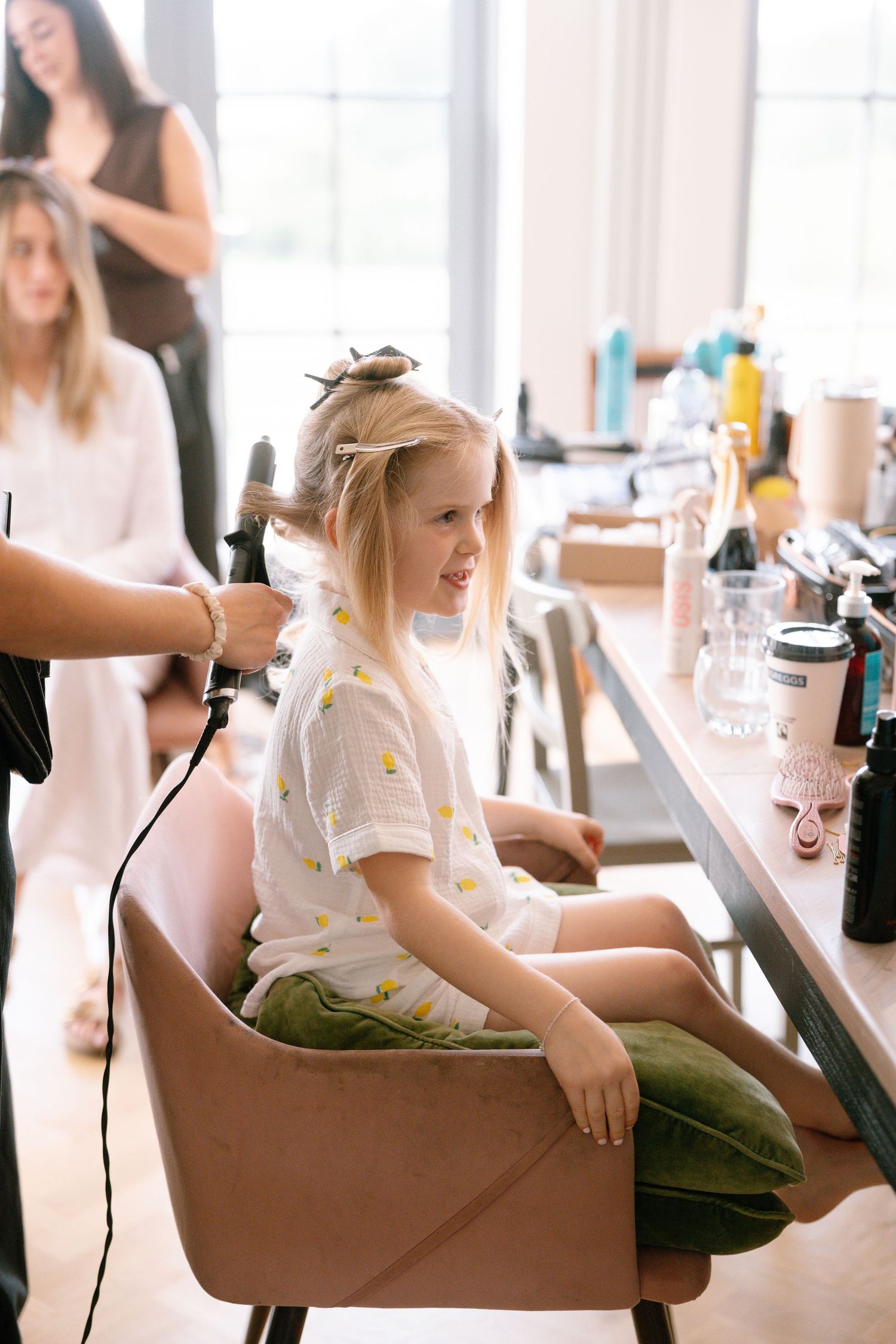 Hair styling session in a bright sunlit room with brown leather chairs.