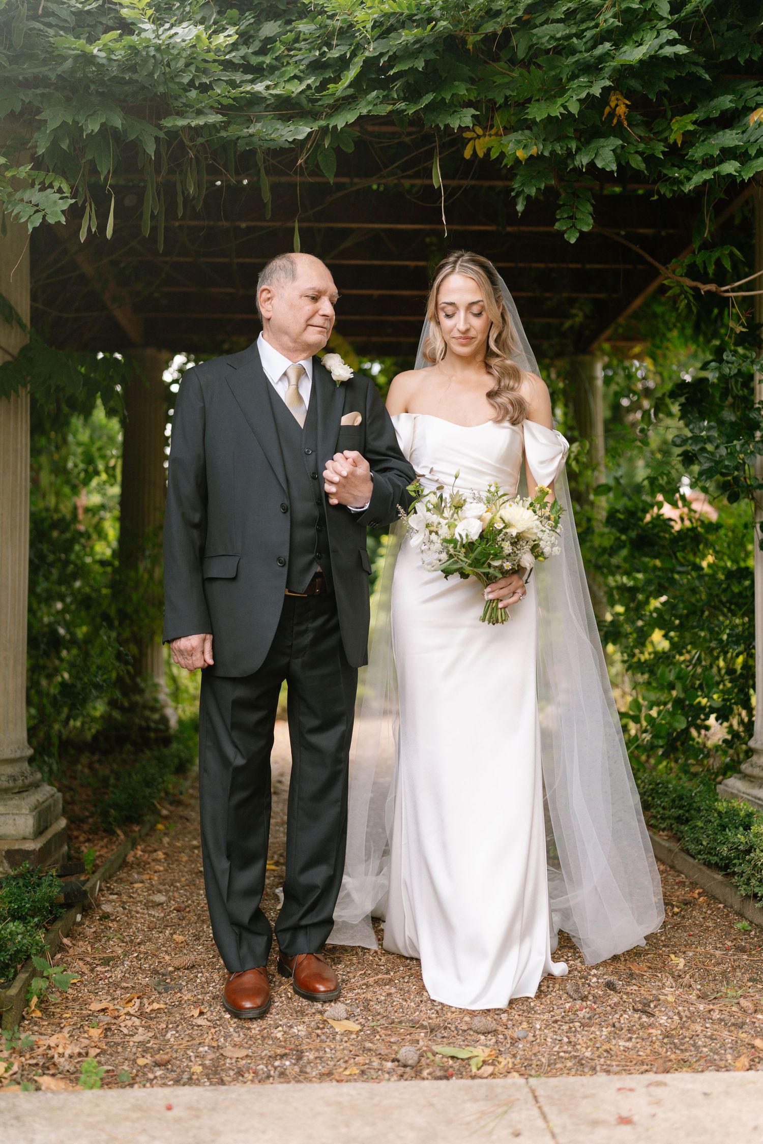 Wedding party walking through a garden pathway under green foliage.