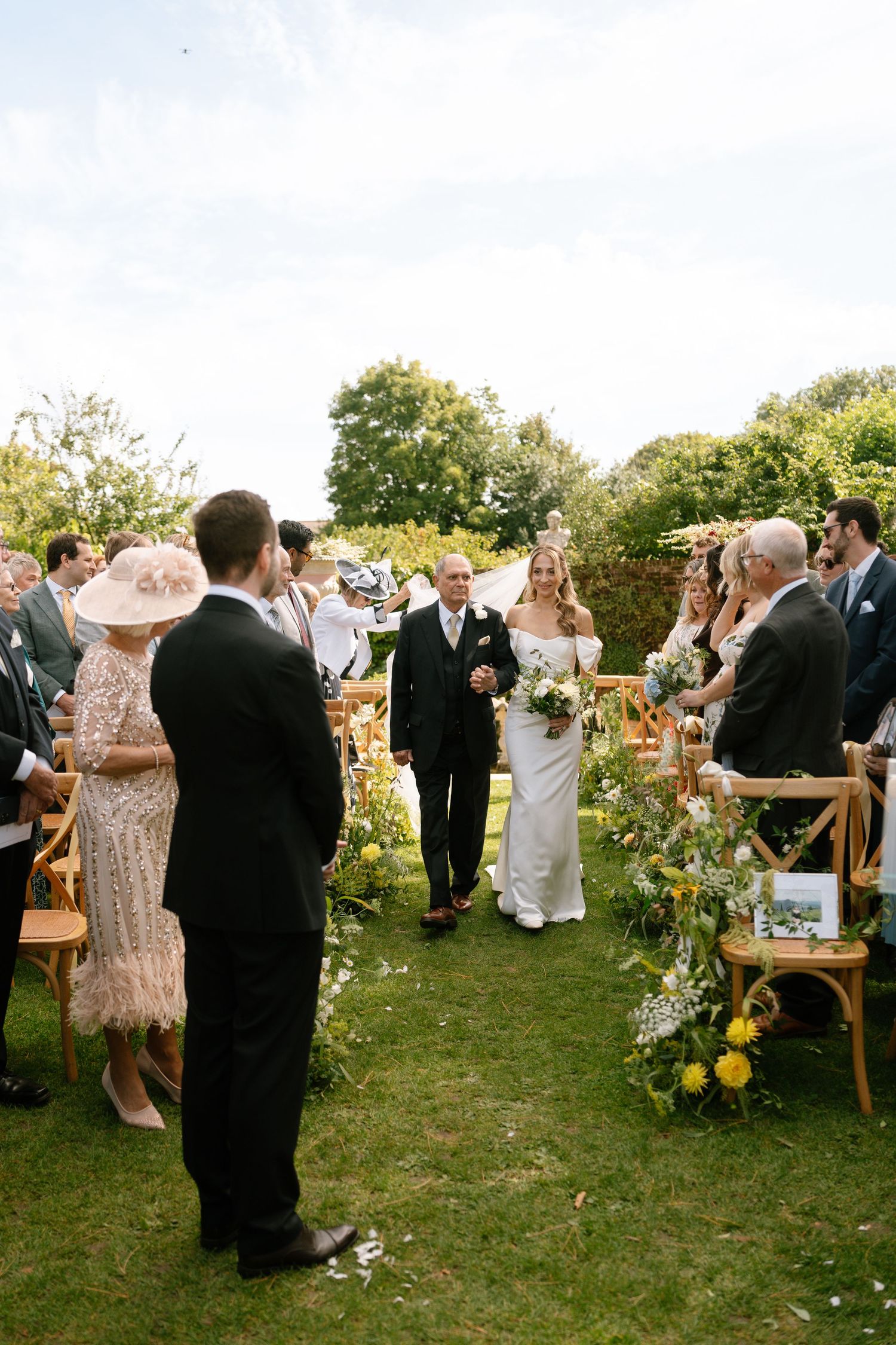Wedding guests socializing on a lawn decorated with flowers and wooden chairs.