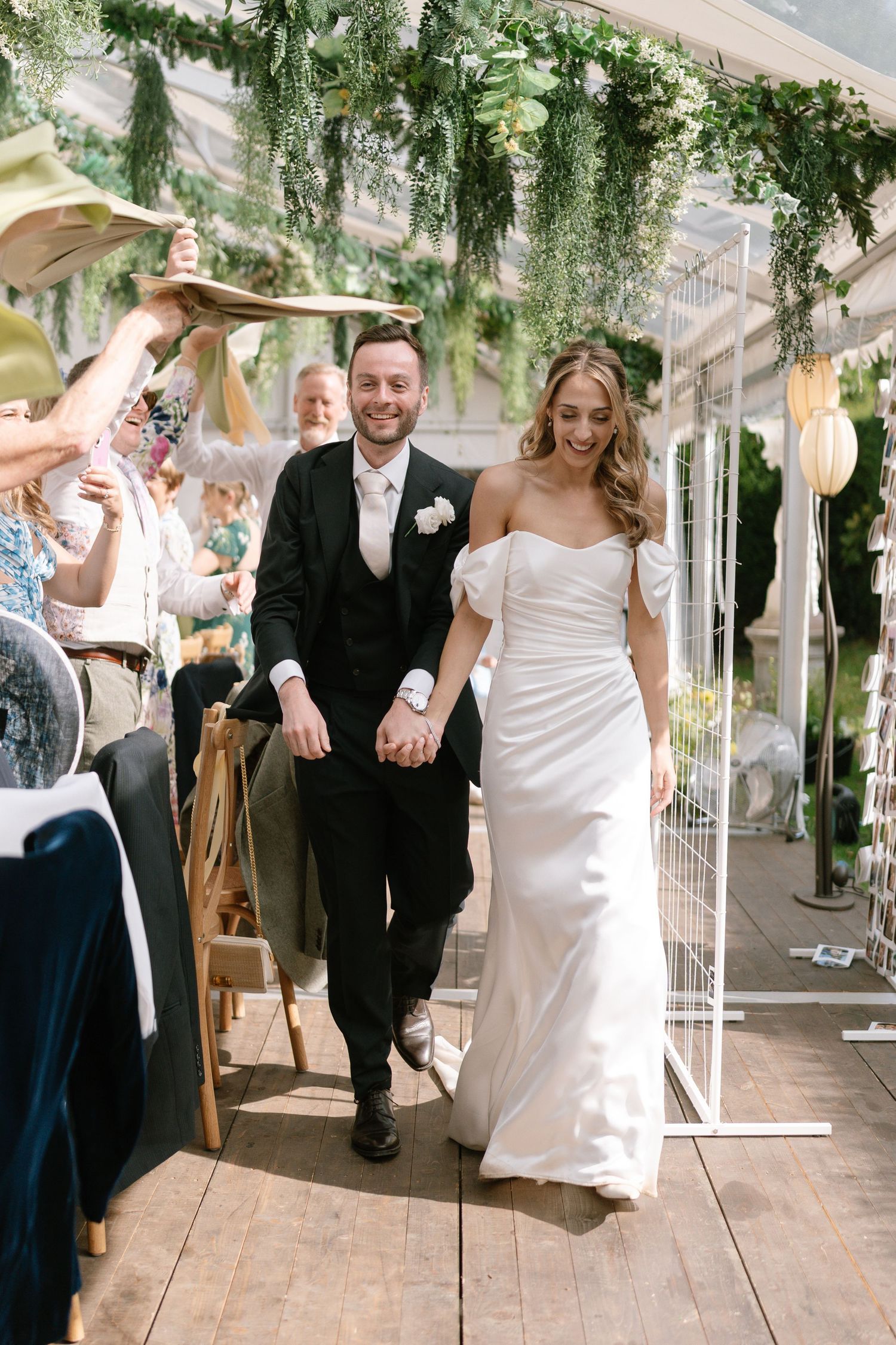 Newlyweds walking through reception tent while guests celebrate.