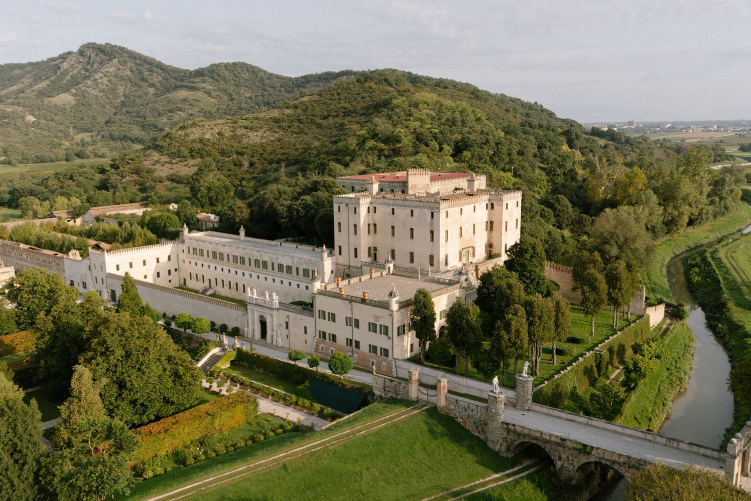 Panoramic aerial view of historic monastery buildings nestled in green hillside landscape.