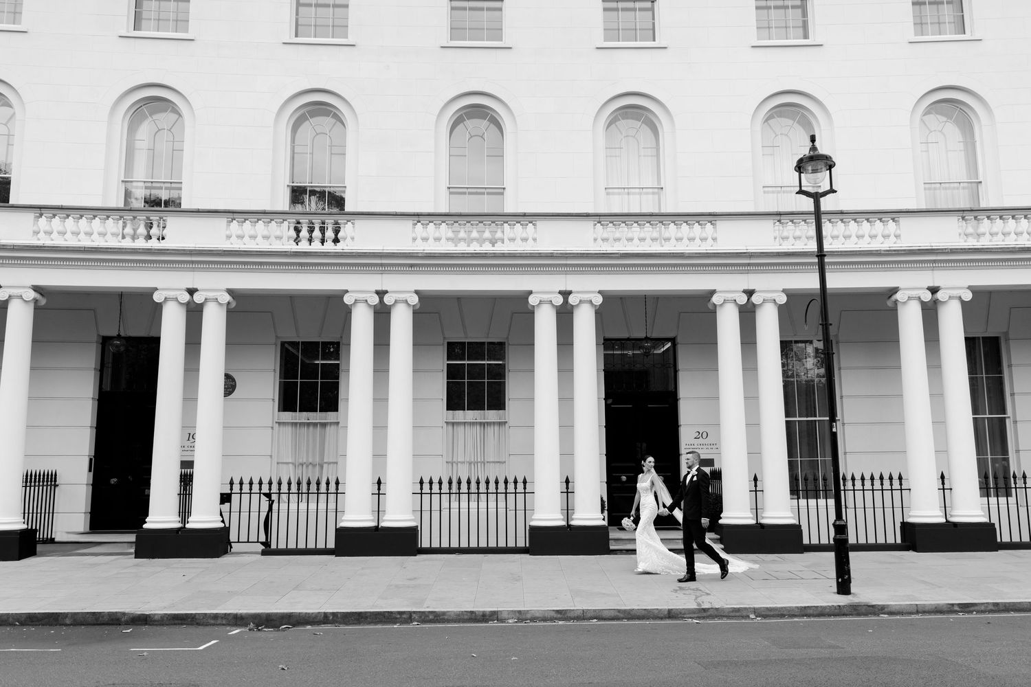 Black and white photo of couple walking past historic London townhouses with white columns.