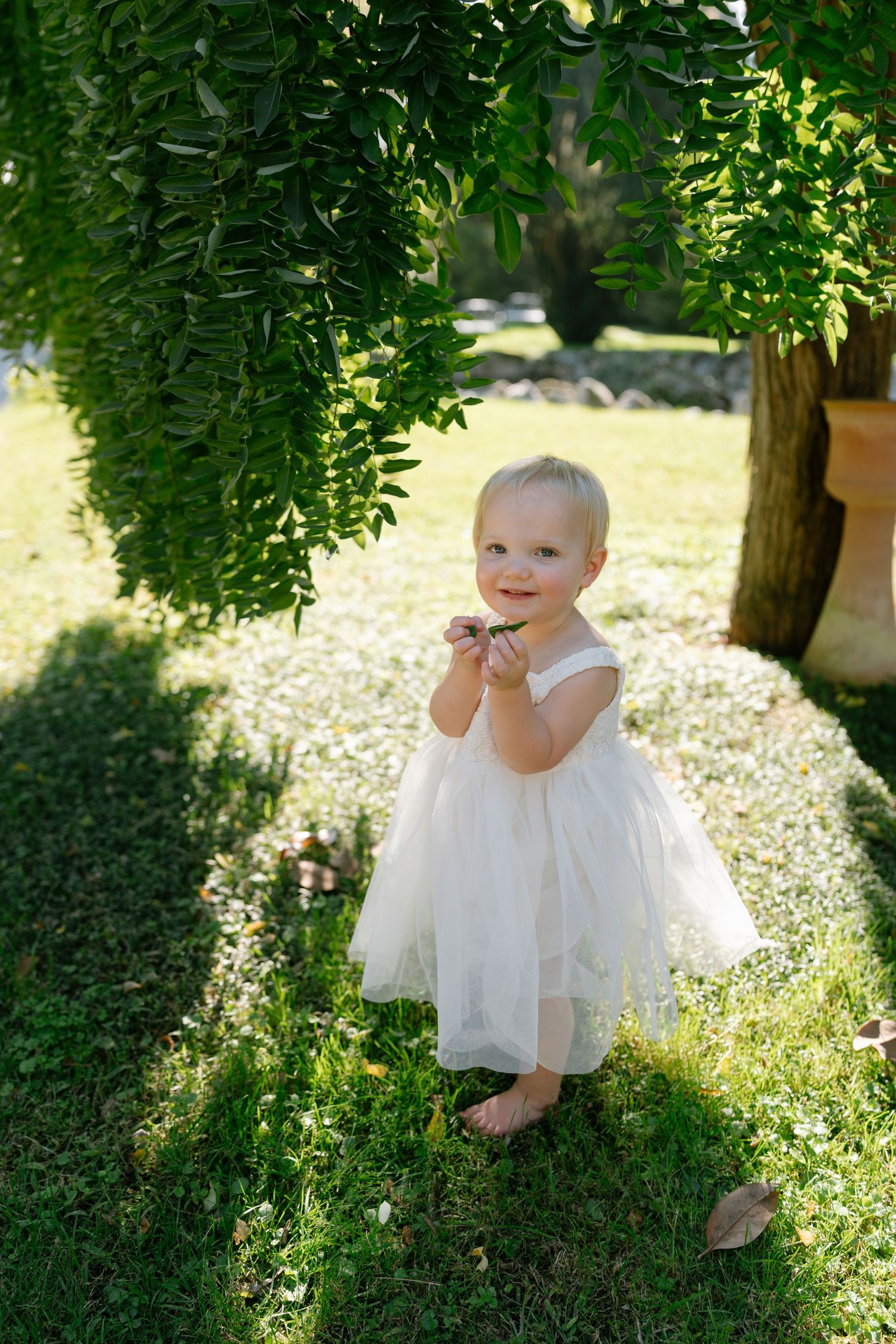 White dress-clad figure plays joyfully under sunlit tree branches.