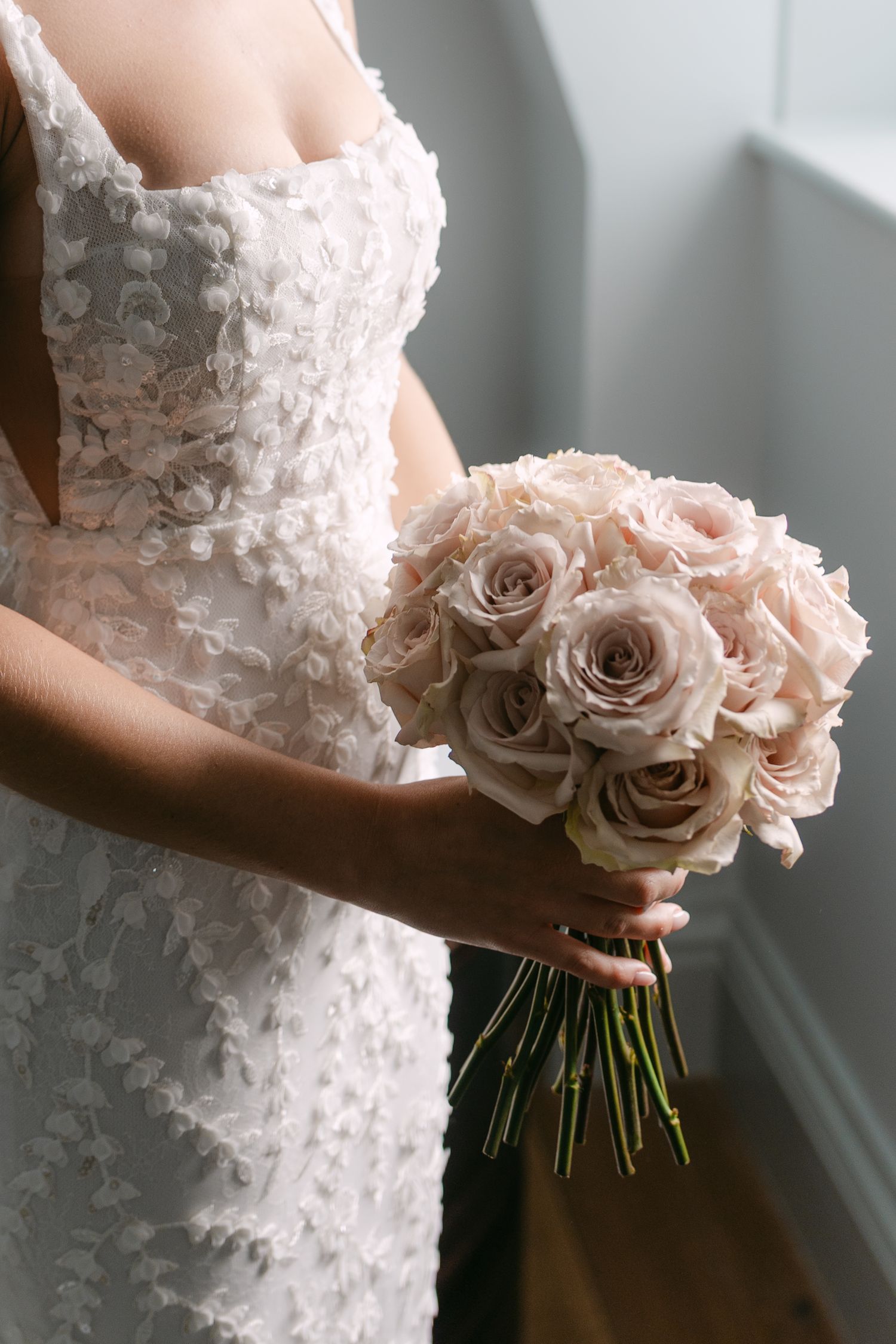 Close-up of blush pink rose bouquet held against white lace wedding dress.