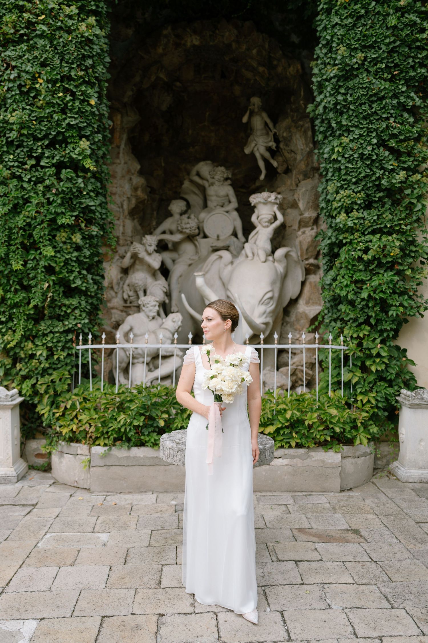 A group poses near stone statues in an ivy-covered garden alcove.