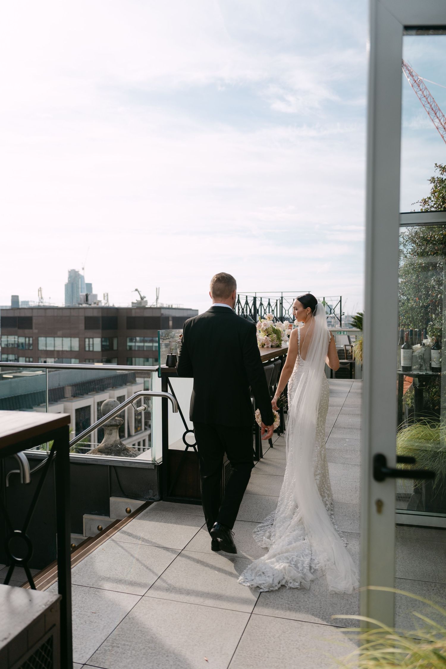 Wedding couple standing on rooftop terrace overlooking city.