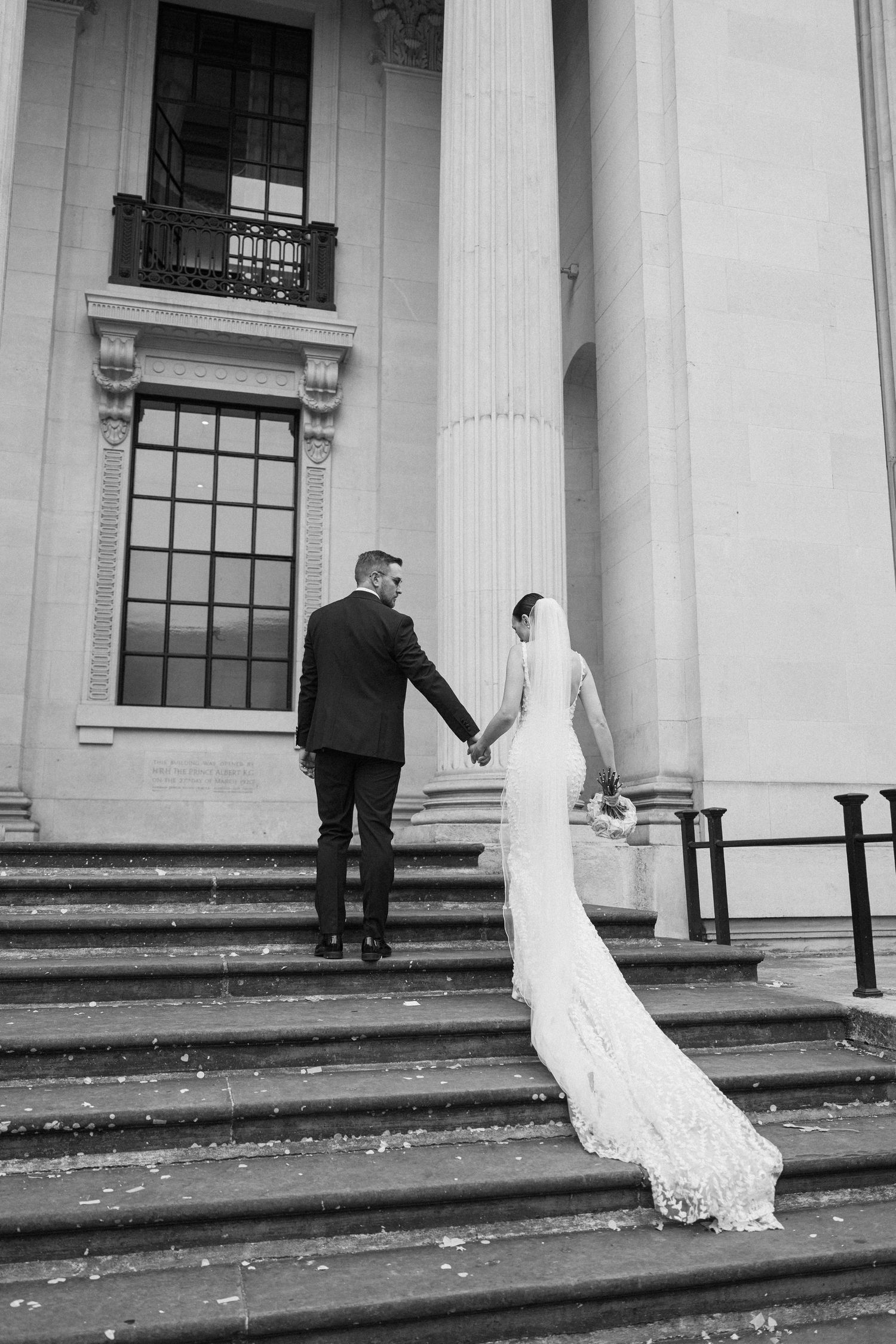 Wedding couple creates artistic poses on grand stone steps of a historic building.
