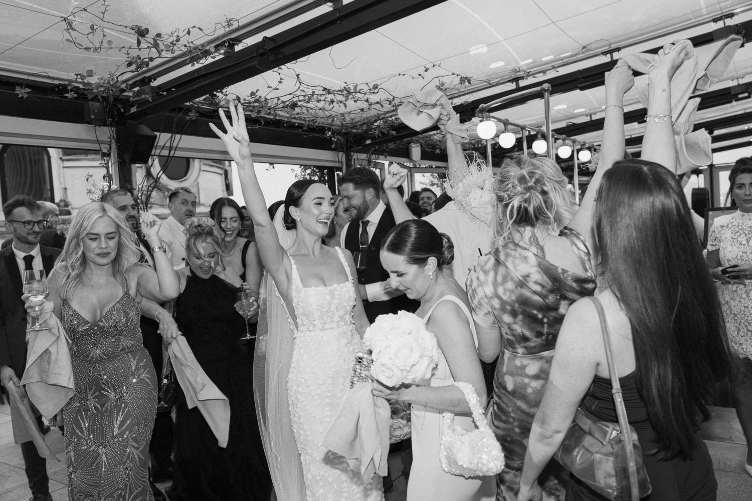 Wedding guests dancing and raising their arms in celebration at a reception.