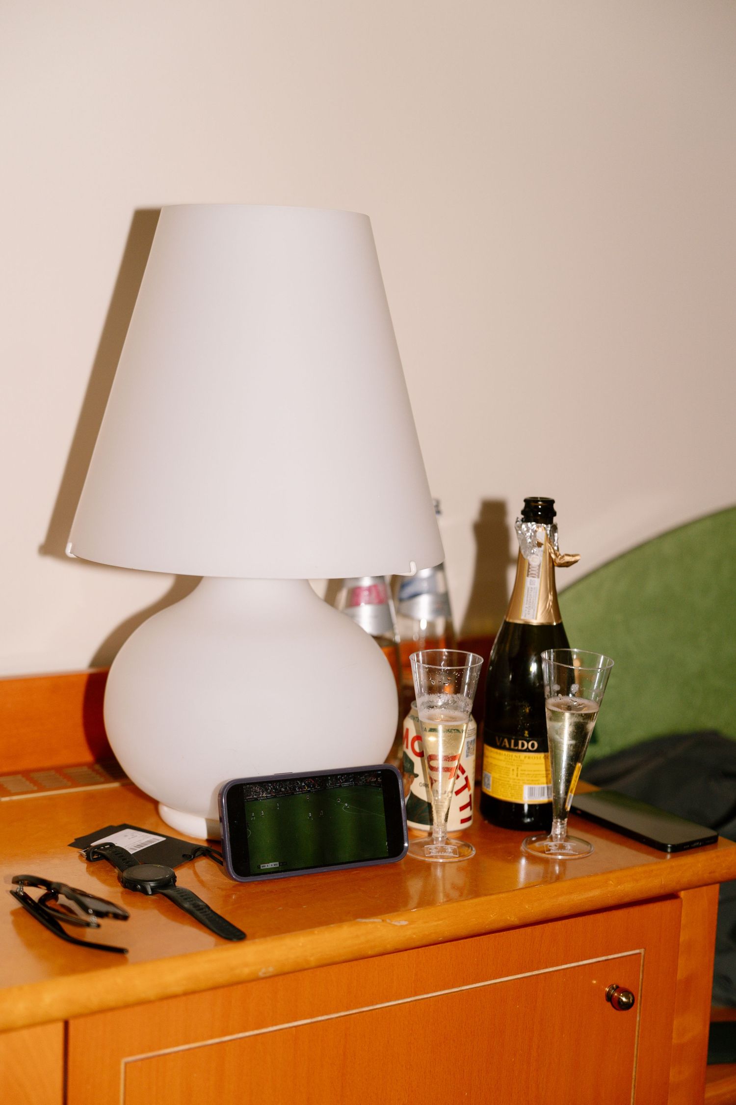 Table lamp and drinks on wooden dresser in hotel room.