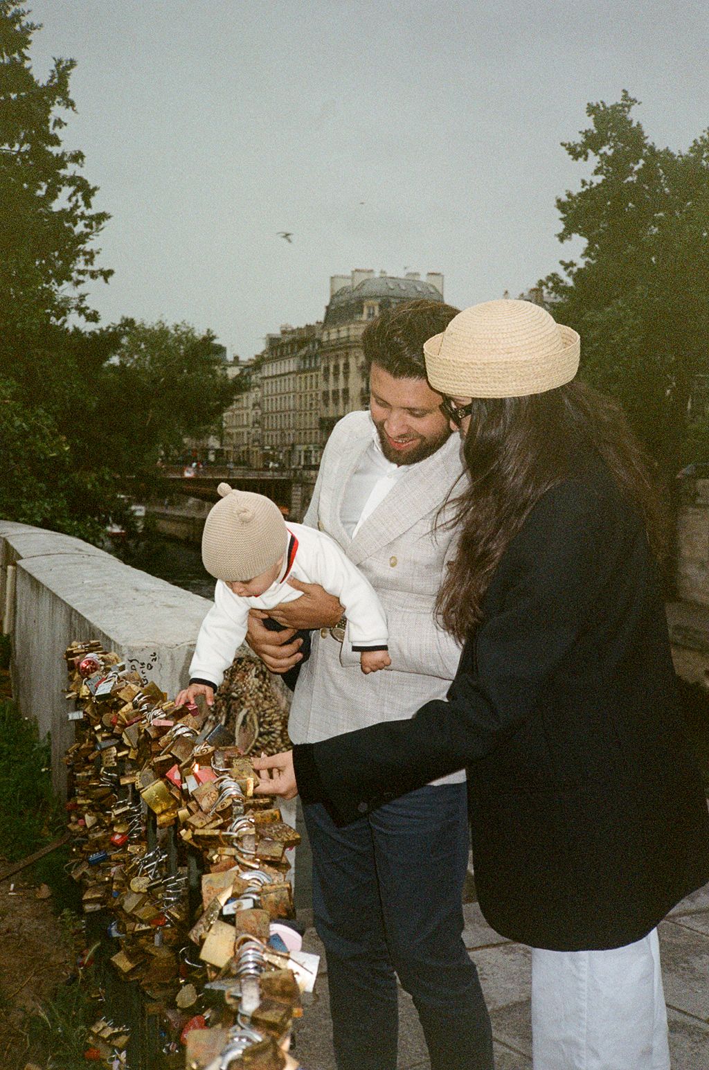 Family with baby attaching love locks to Pont des Arts bridge in Paris, France.