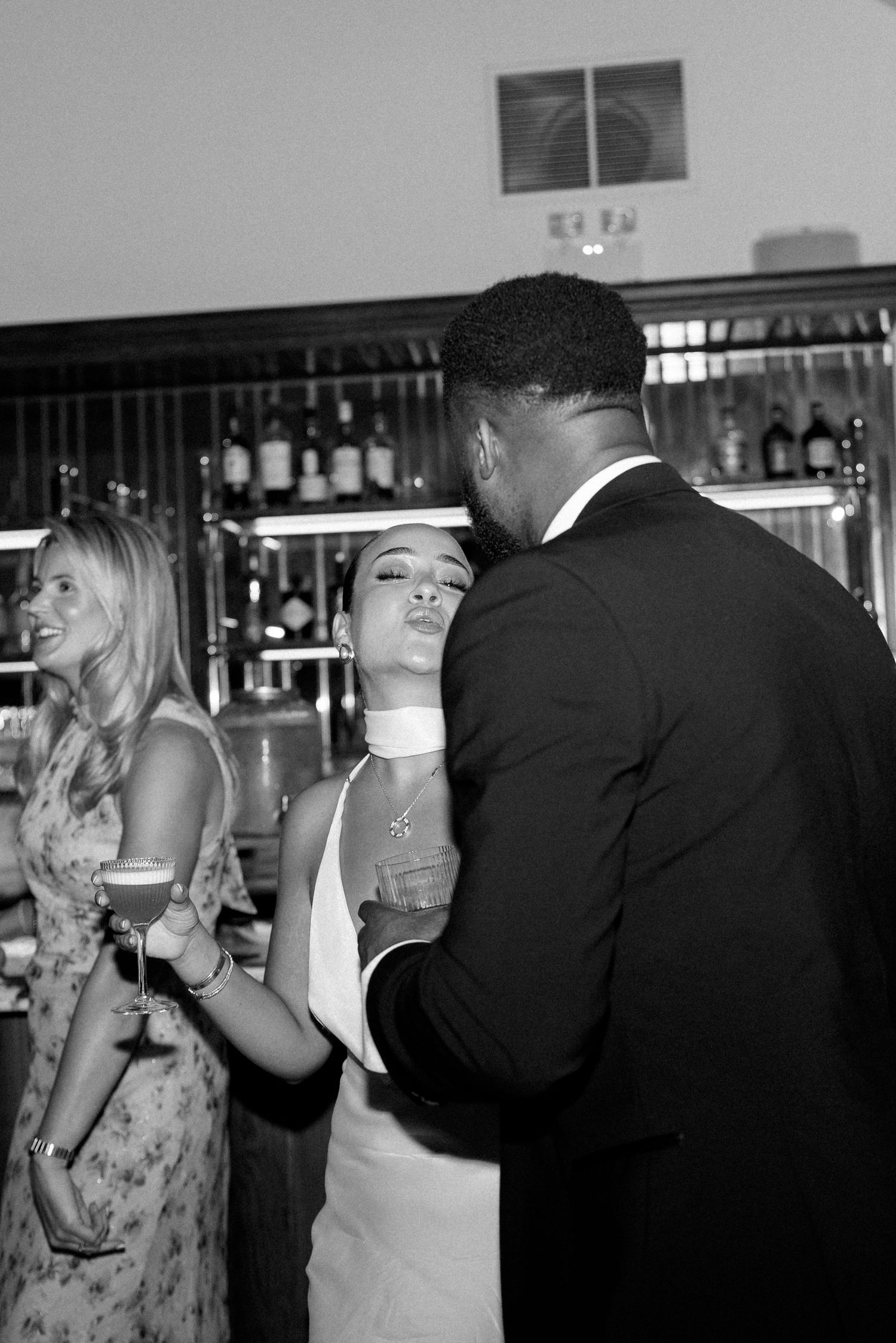 Bride in white gown sharing an intimate moment with groom near a bar at their wedding reception.