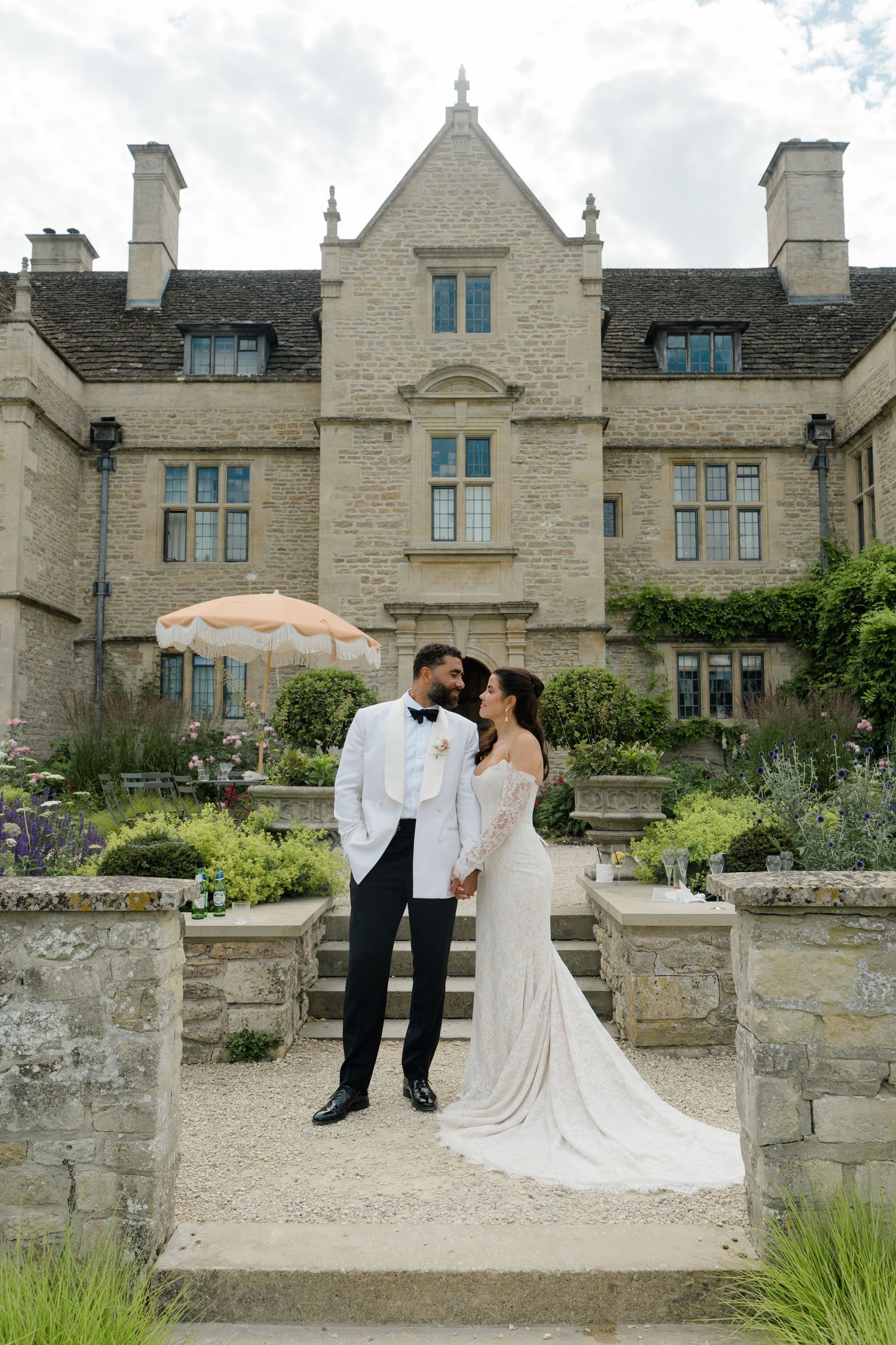 Bride and groom posing together in front of a stunning English manor house wedding venue with lush gardens.