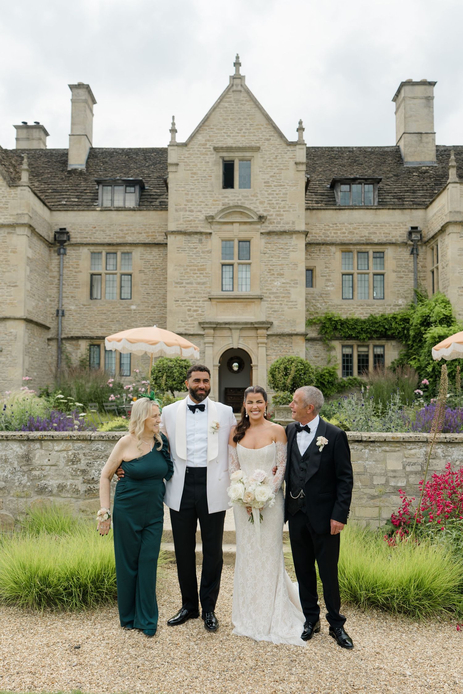 Bride and groom pose with family in front of a grand stone manor house wedding venue.