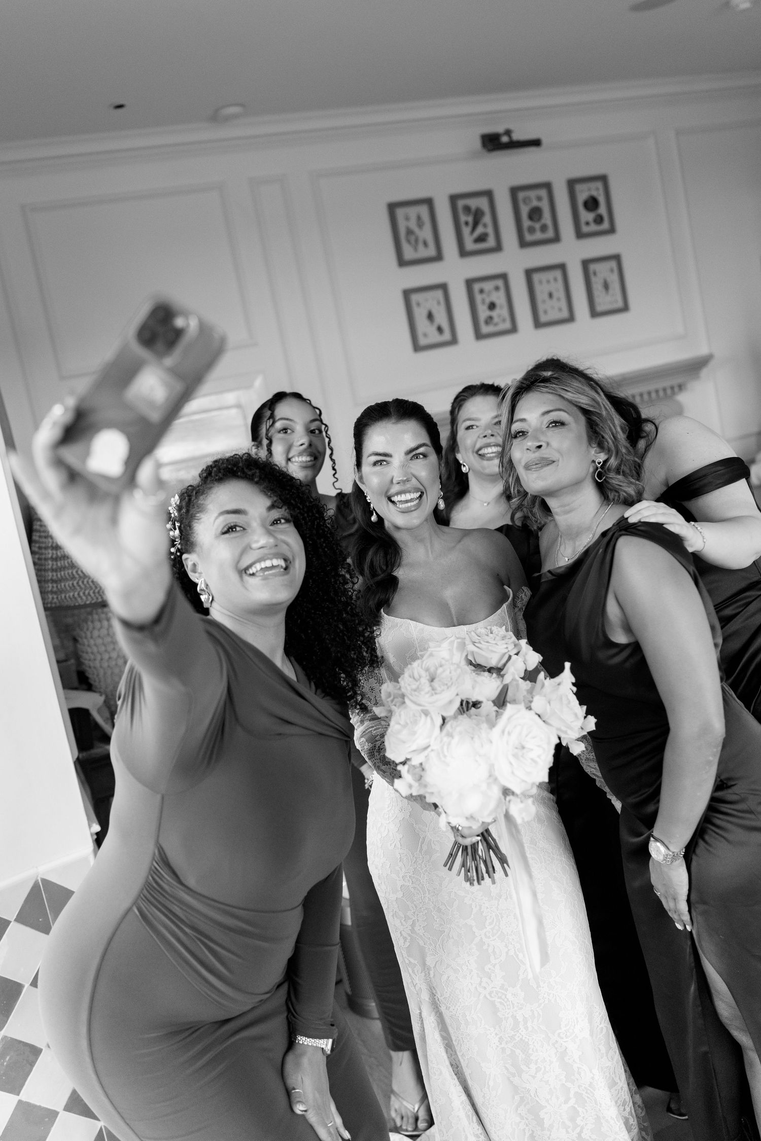 Bride with bouquet takes selfie with bridesmaids in black and white photo.