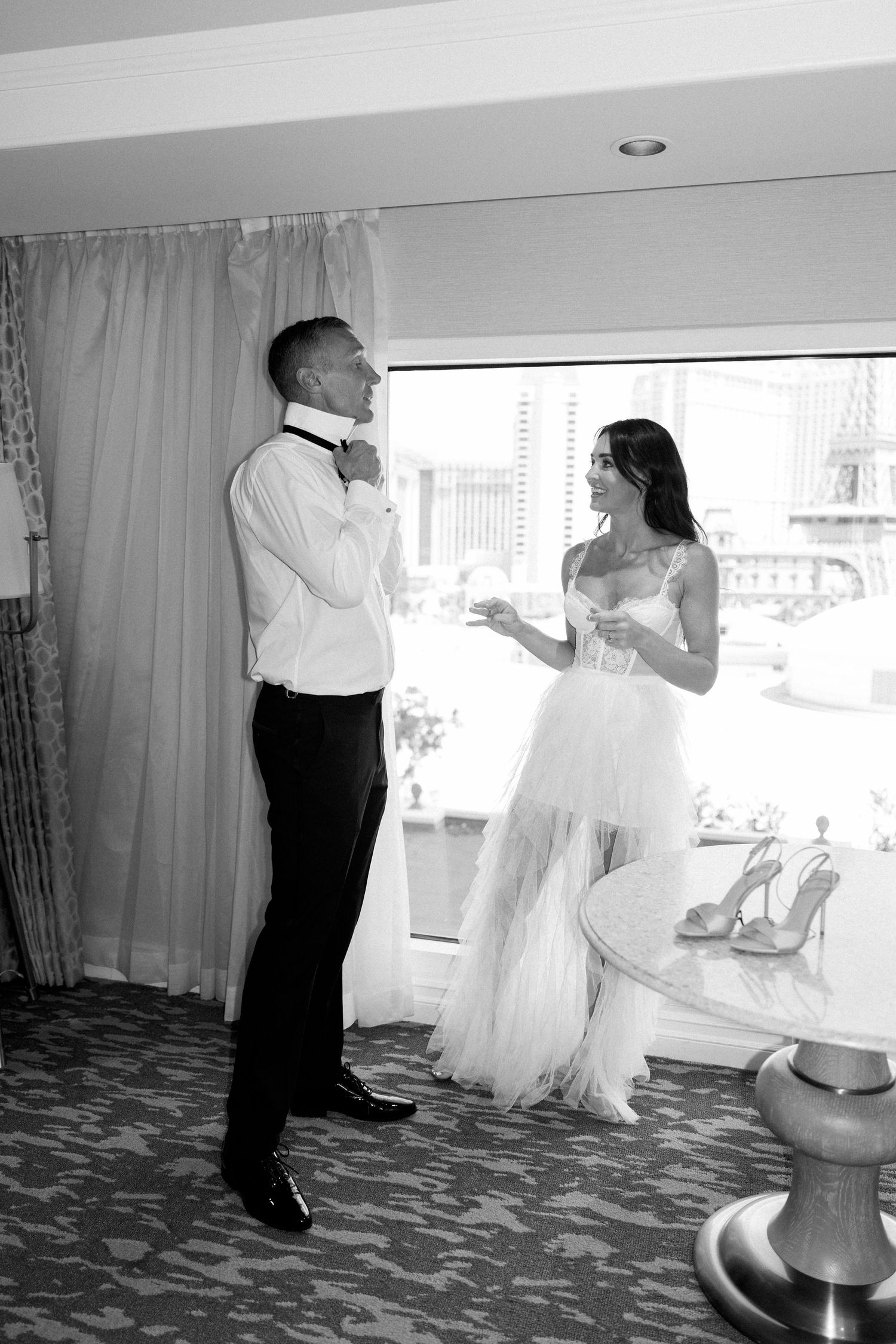 A couple shares a candid moment in a hotel room, with the bride wearing a tulle gown.