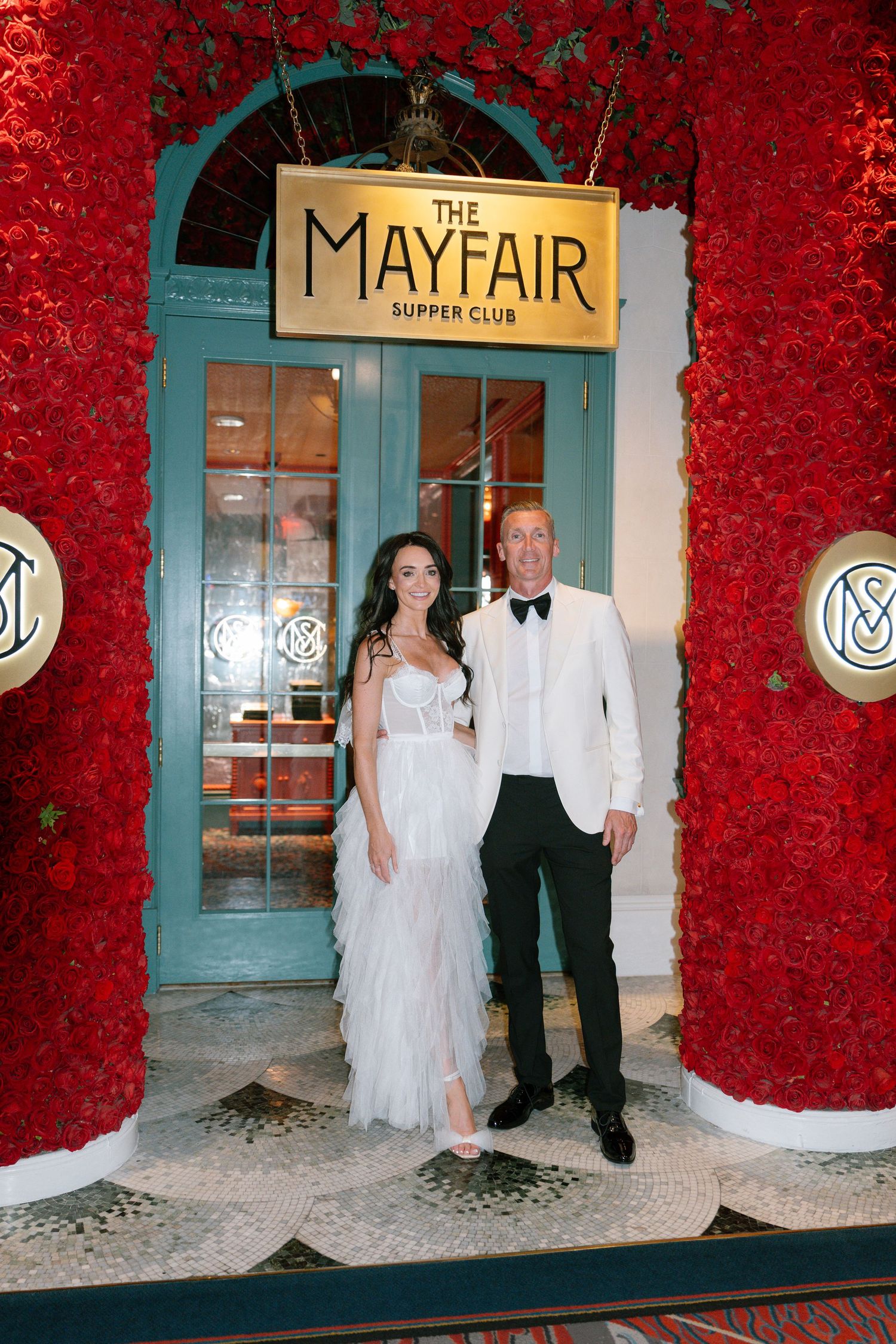 Wedding couple posing in front of The Mayfair Supper Club entrance decorated with red roses.