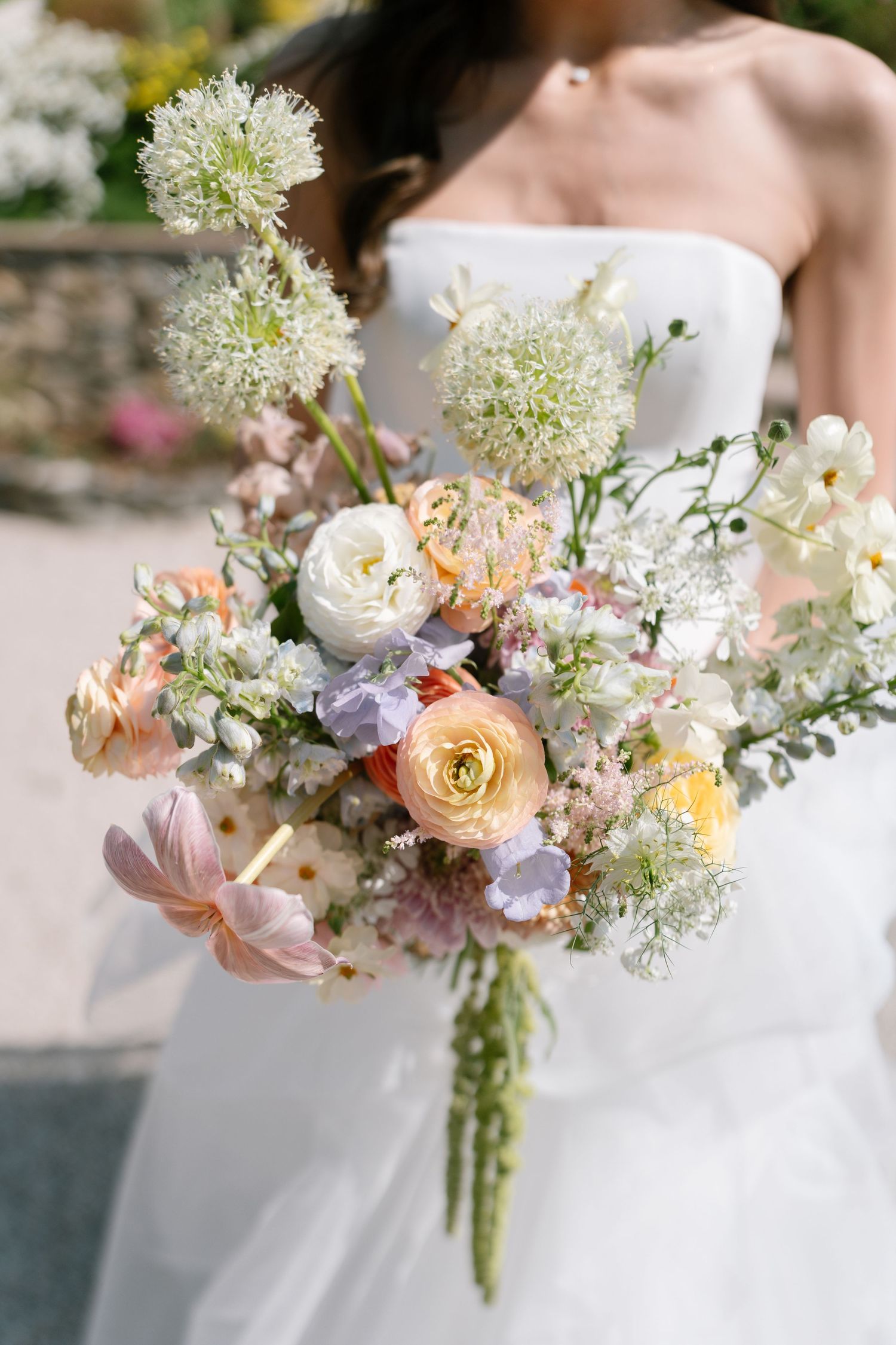 A delicate pastel wedding bouquet with roses, ranunculus and wildflowers against a white dress.