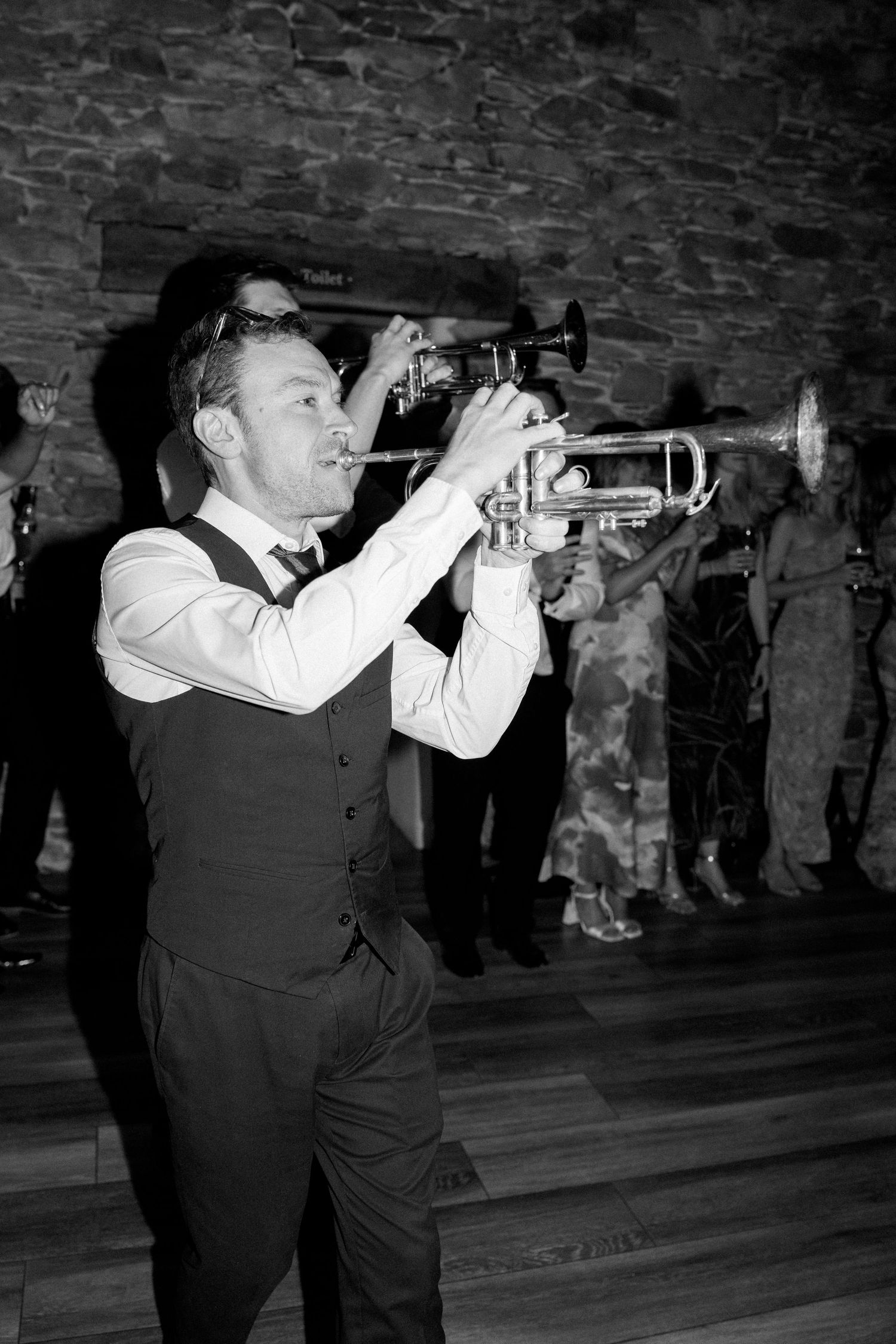 Musicians perform with trumpets at a wedding reception in a rustic stone venue.