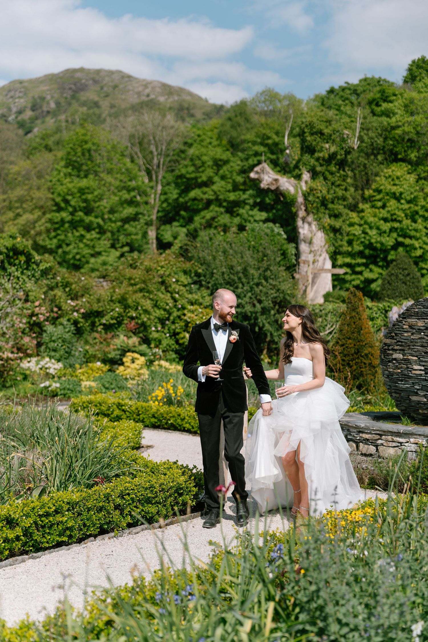 Wedding couple enjoying champagne in a terraced garden with mountain views and blooming flowers.