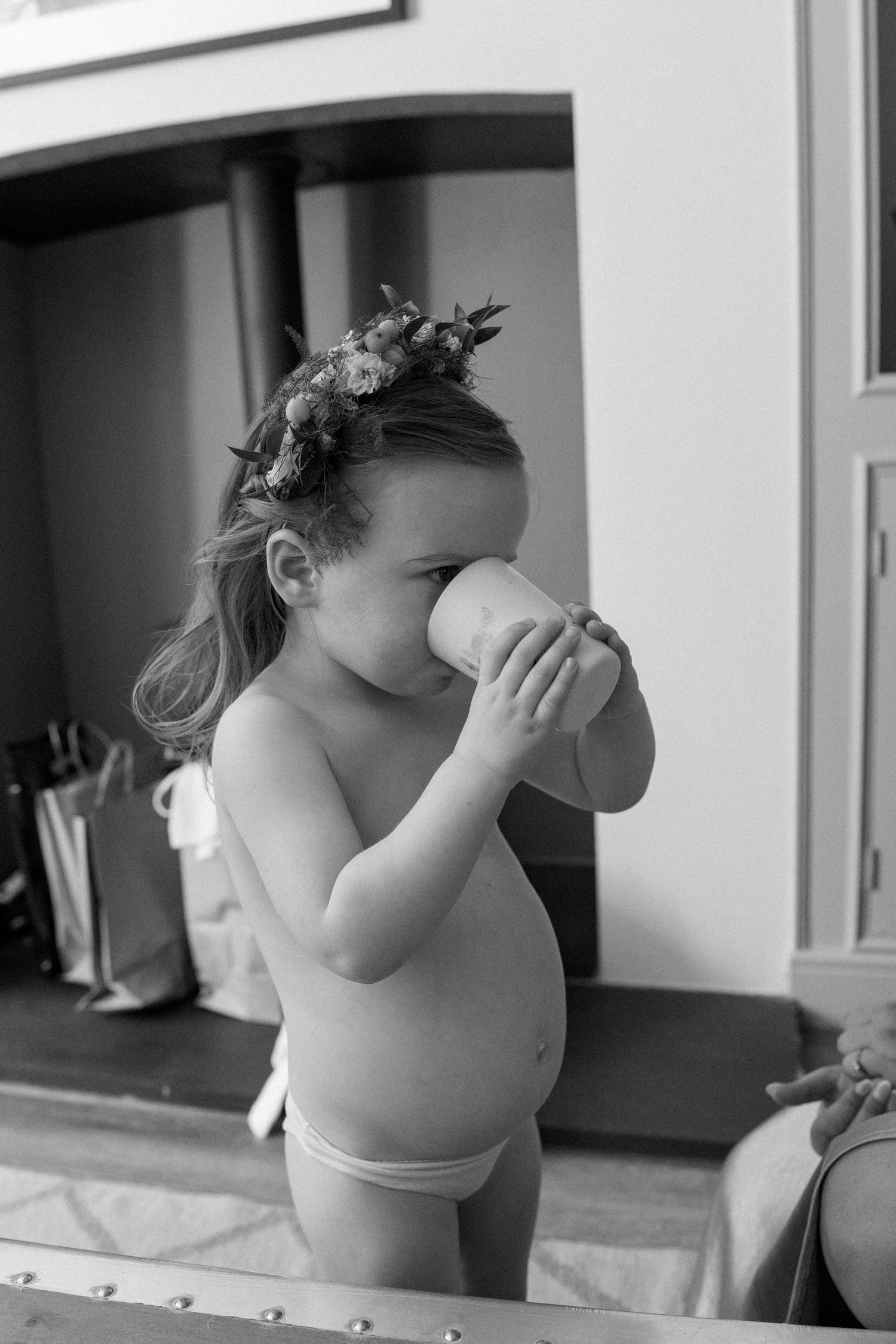 Small child in white drinking from a cup against a light background.