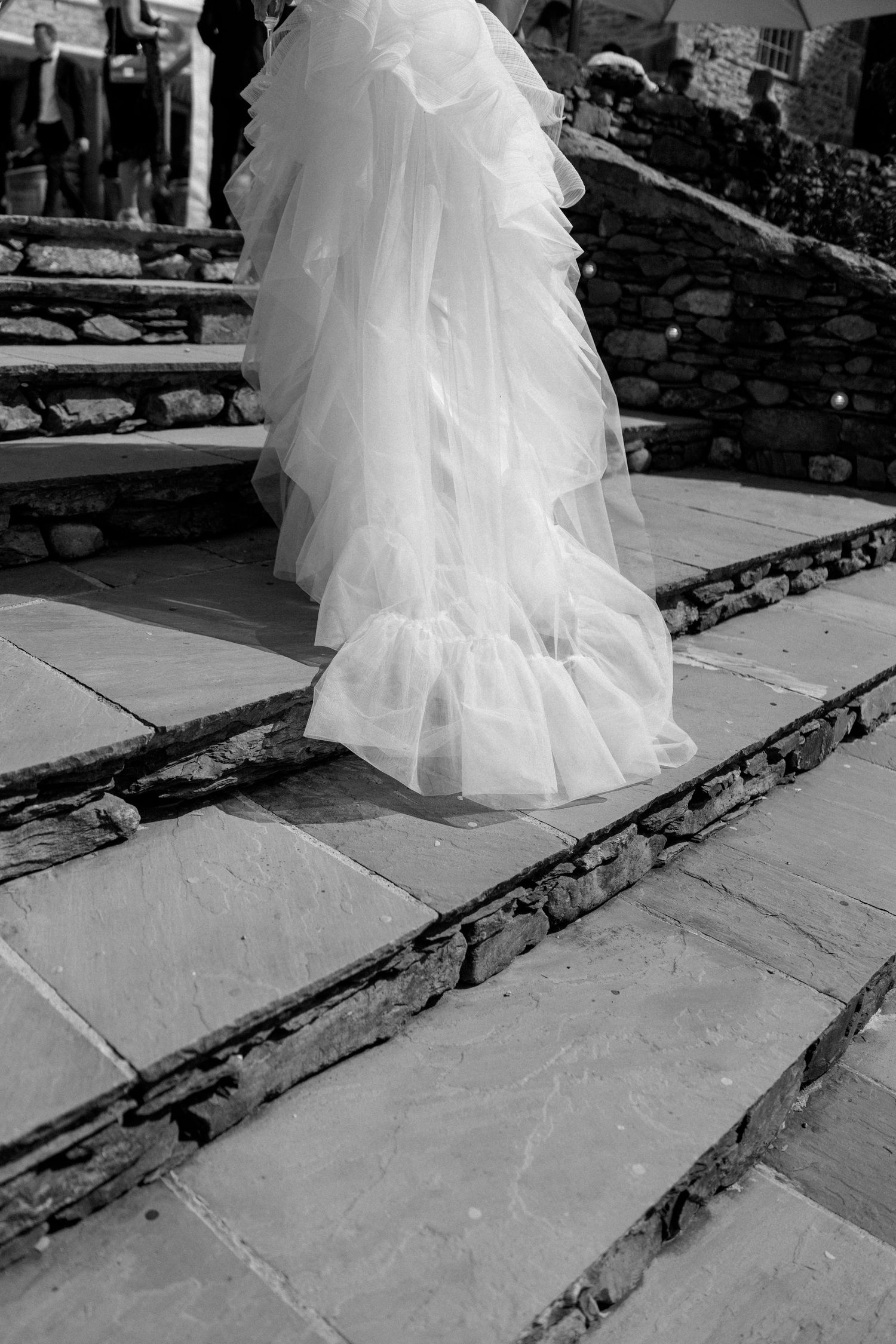 Close-up of a flowing white wedding dress as couple walks up stone steps.