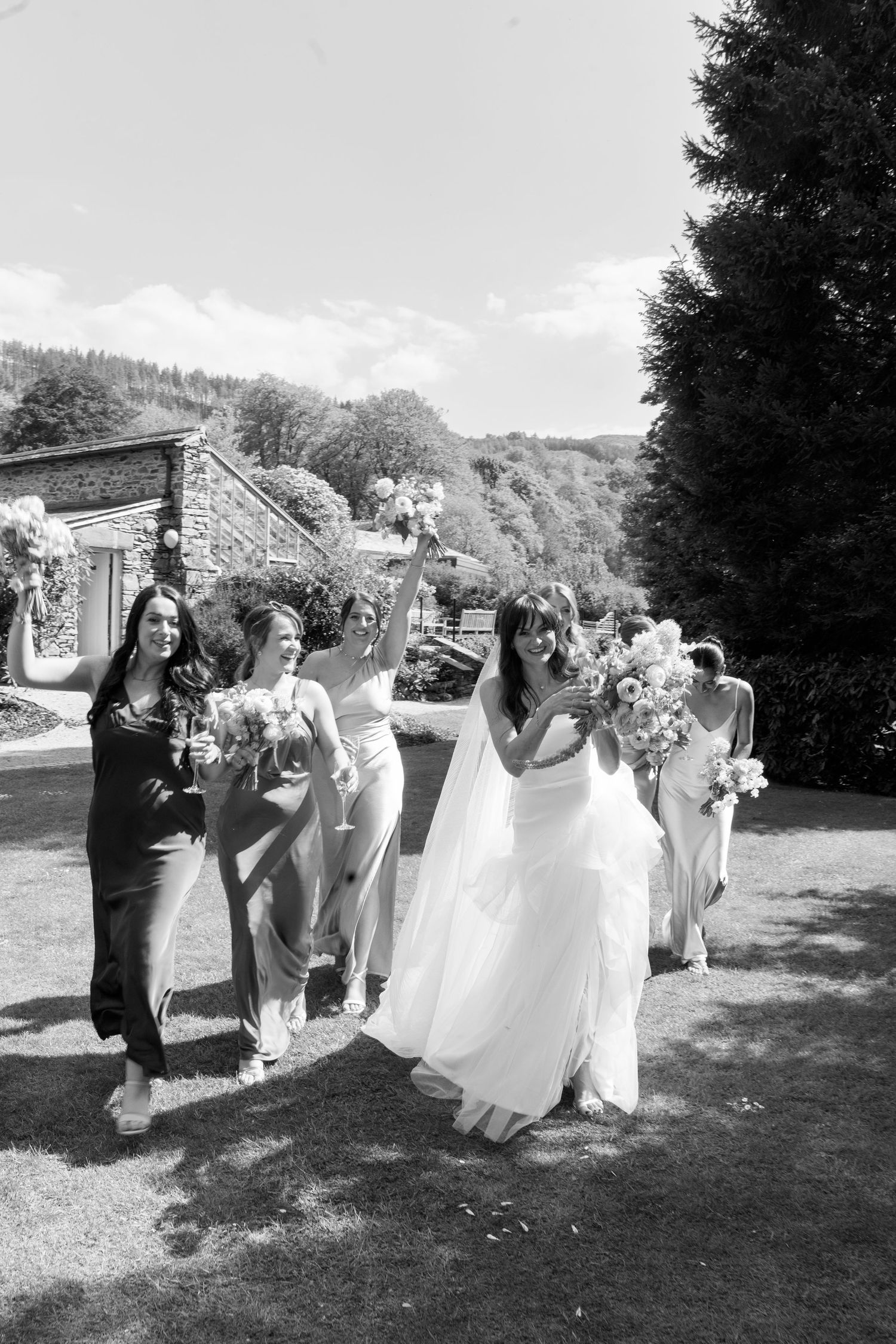 Wedding party walks together on a grassy path during an outdoor celebration.