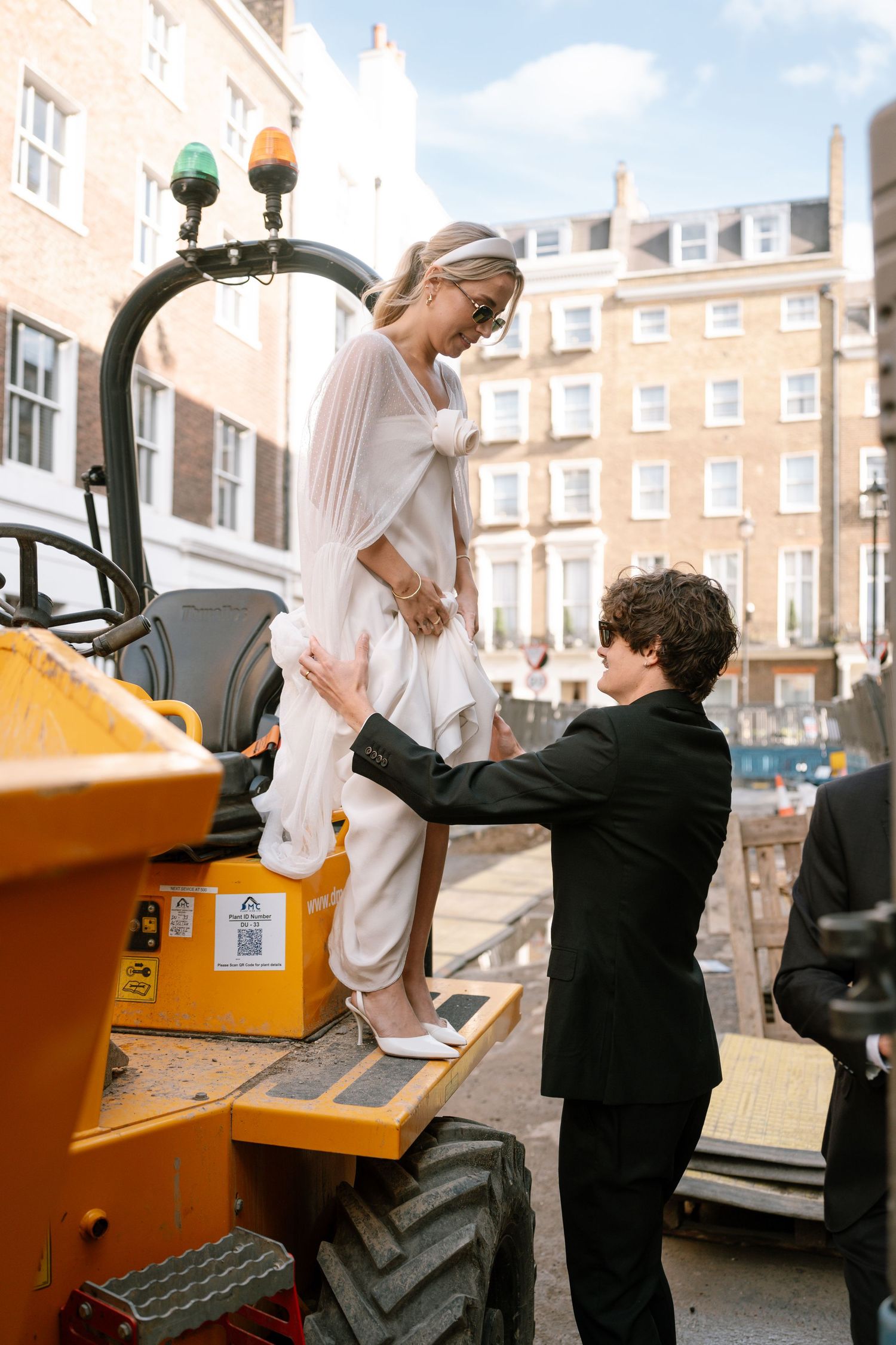 Wedding couple climbs onto a bright yellow construction vehicle for photos.