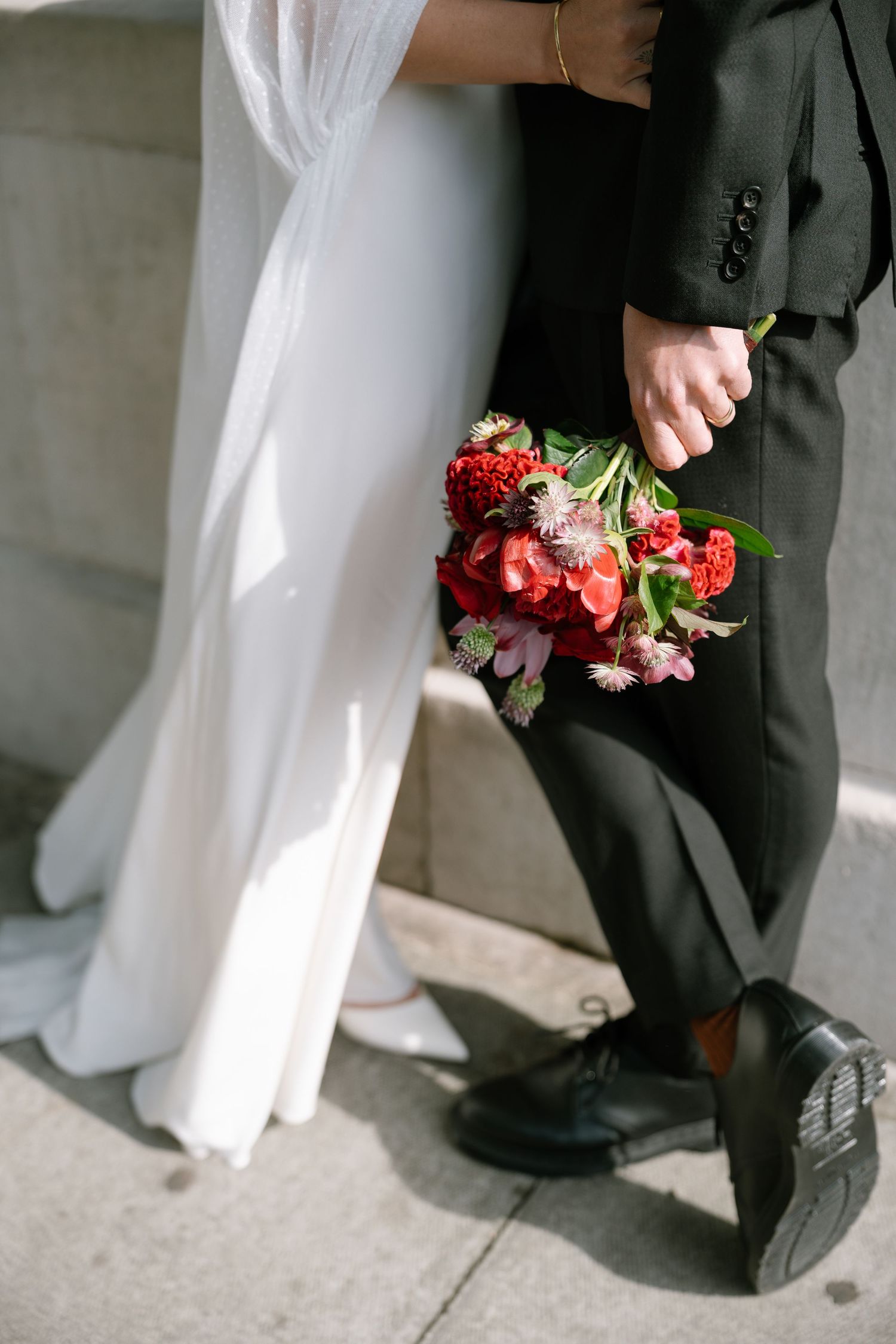 Close-up of wedding couple's feet and red bouquet against stone steps and columns.
