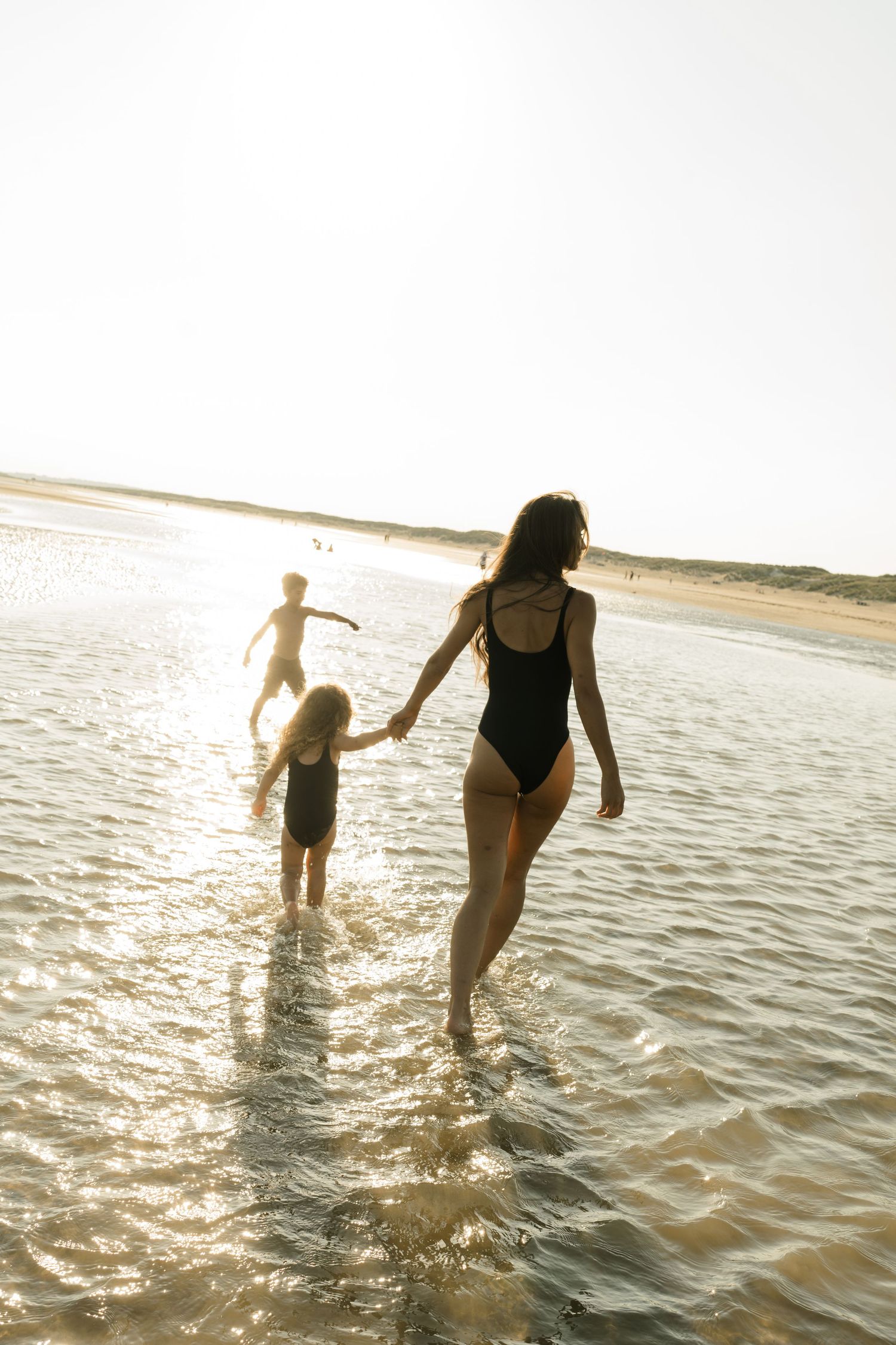 Two people splash and play in shallow ocean water at sunset creating silhouettes against the glowing horizon.