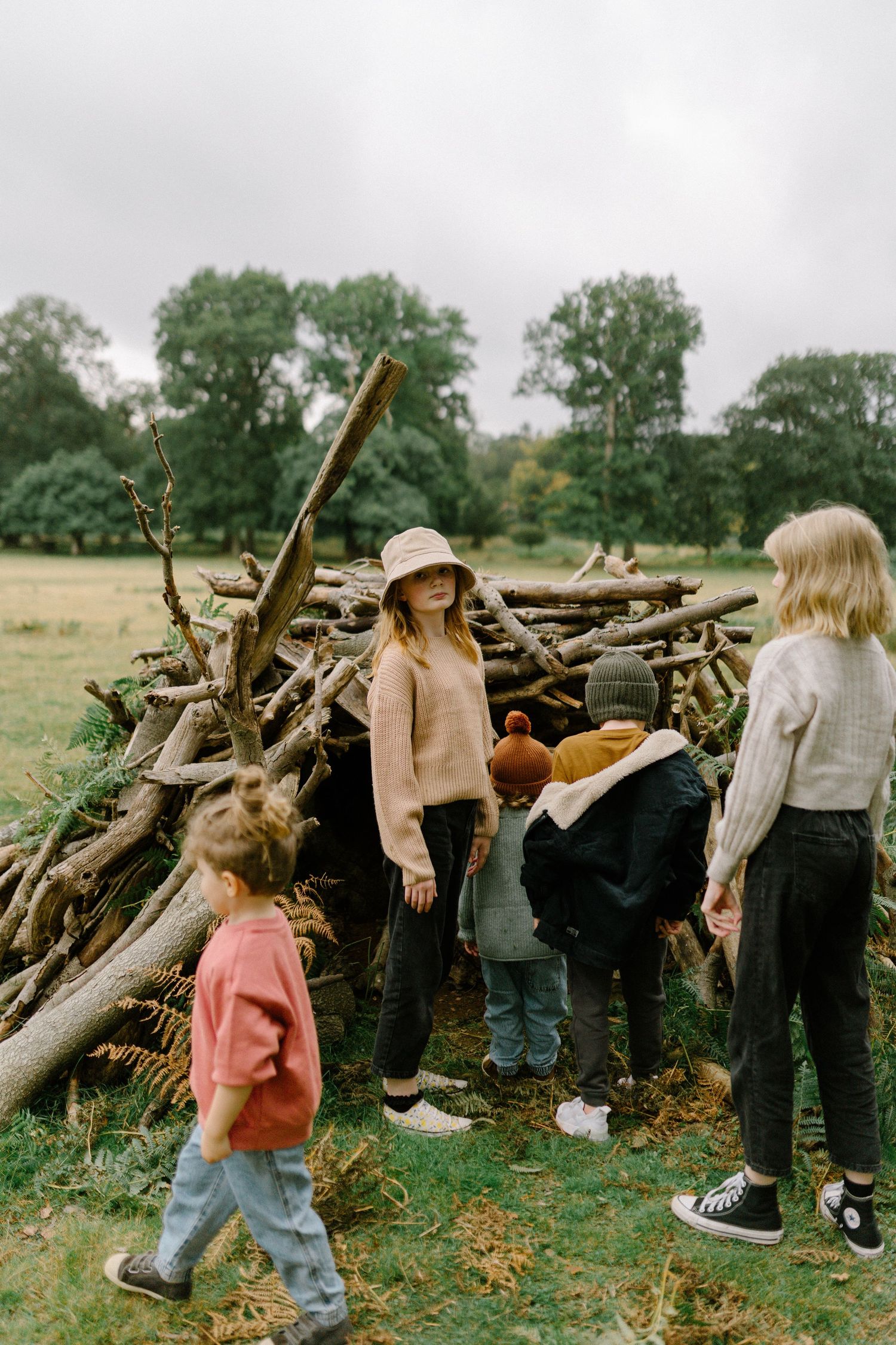 A group explores a woodpile on an overcast day wearing autumn sweaters and boots.