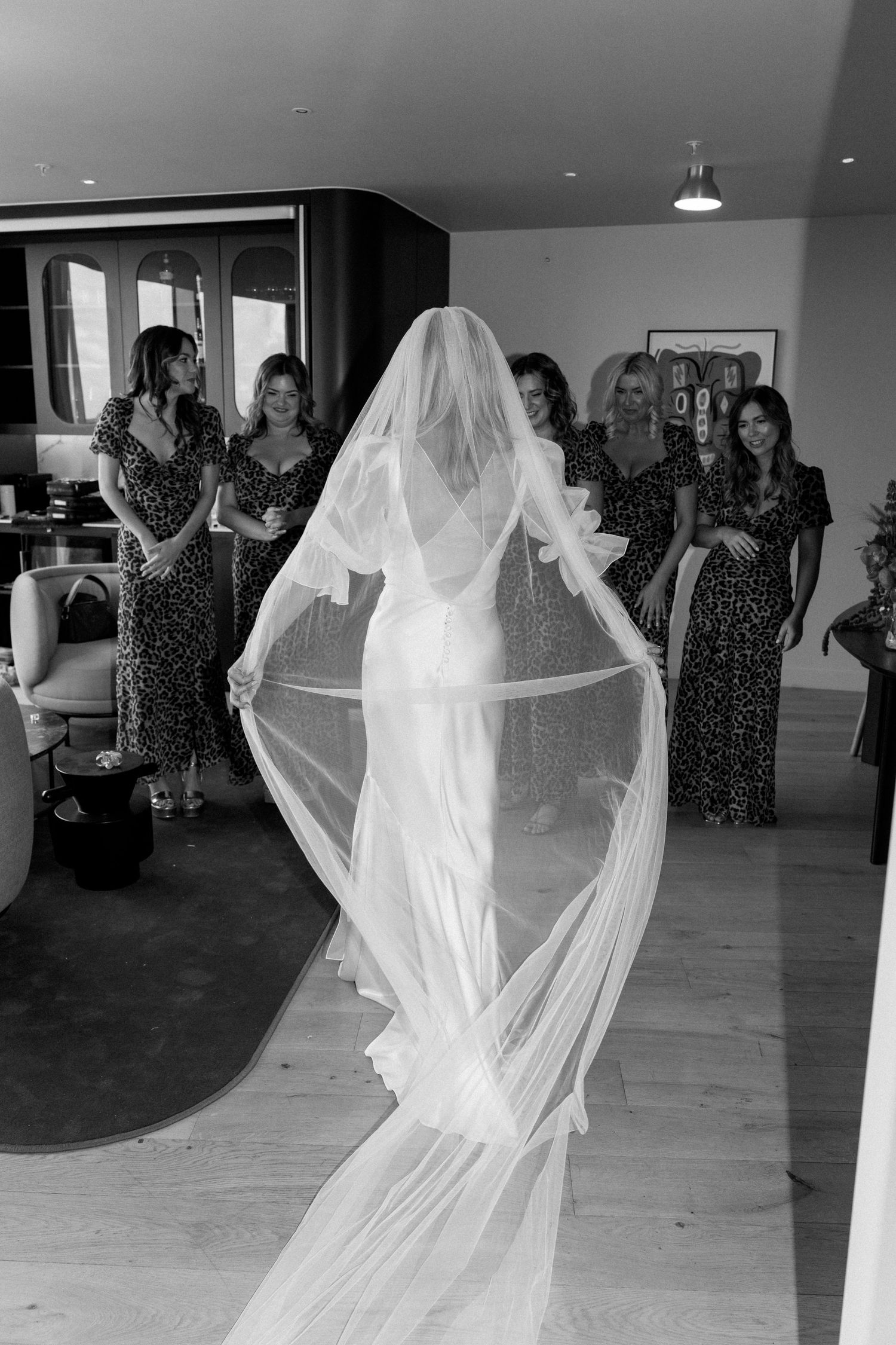 Bride in flowing veil and fitted white dress reveals her look to bridesmaids.