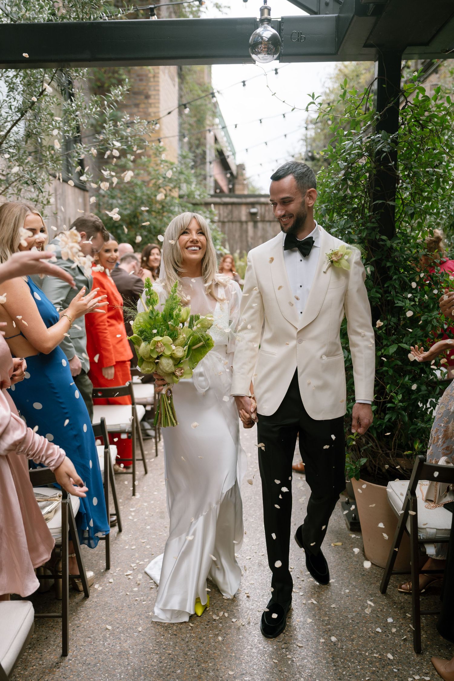 Wedding party celebrates with joyful dancing in an outdoor garden venue.