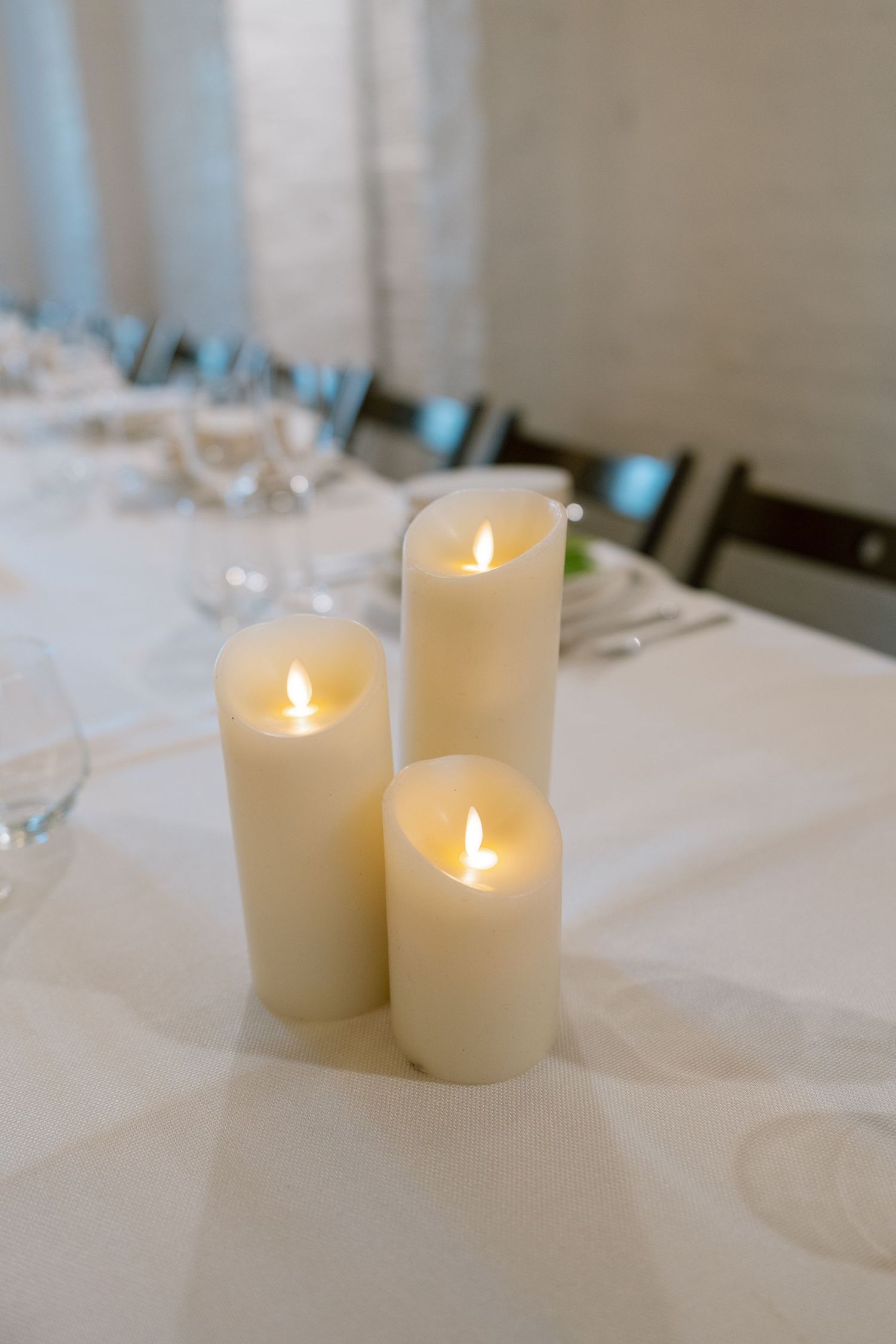 White pillar candles glowing on an elegant table setting with white linens.