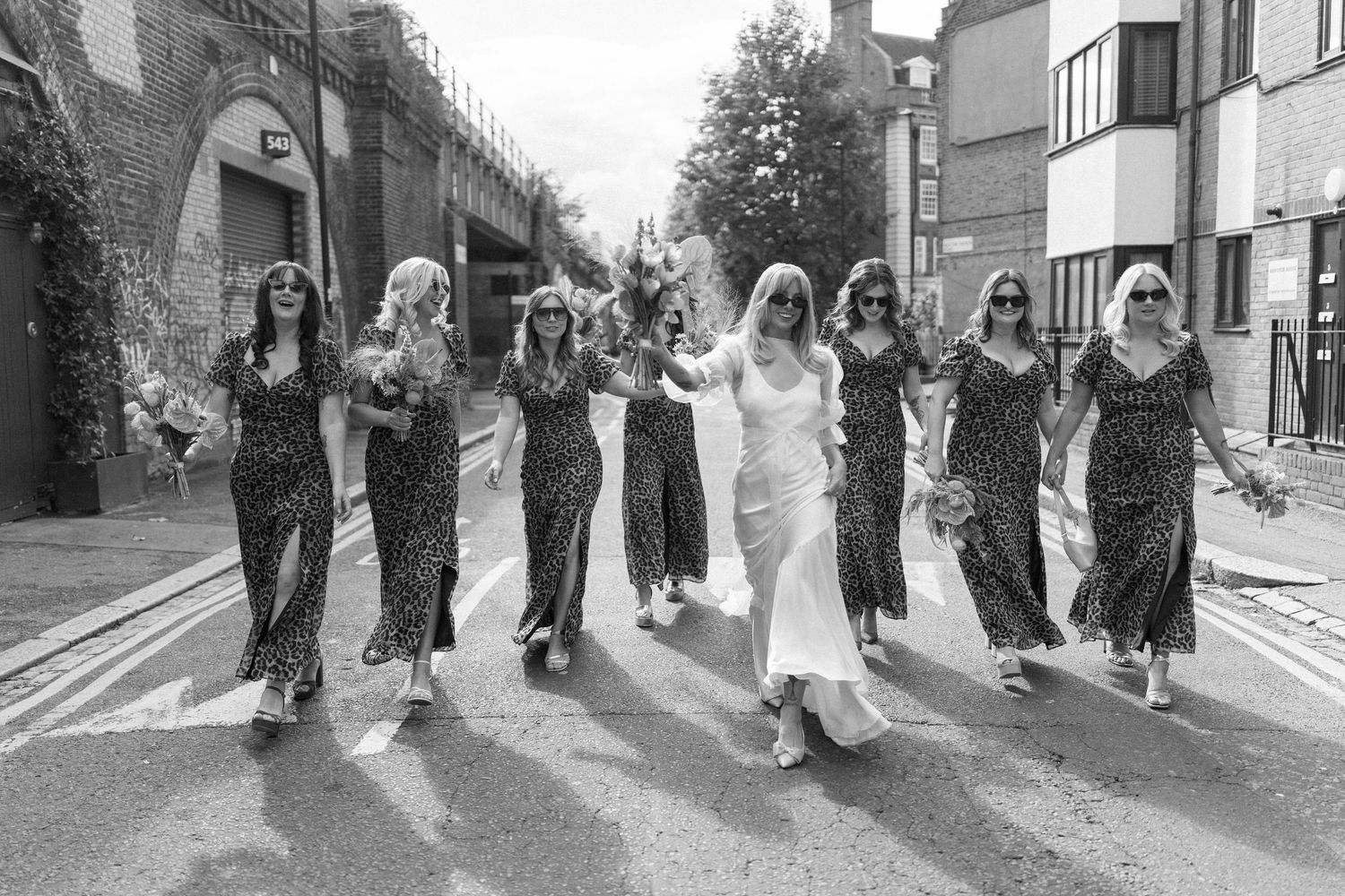 A wedding party walking together down a street in formal attire.