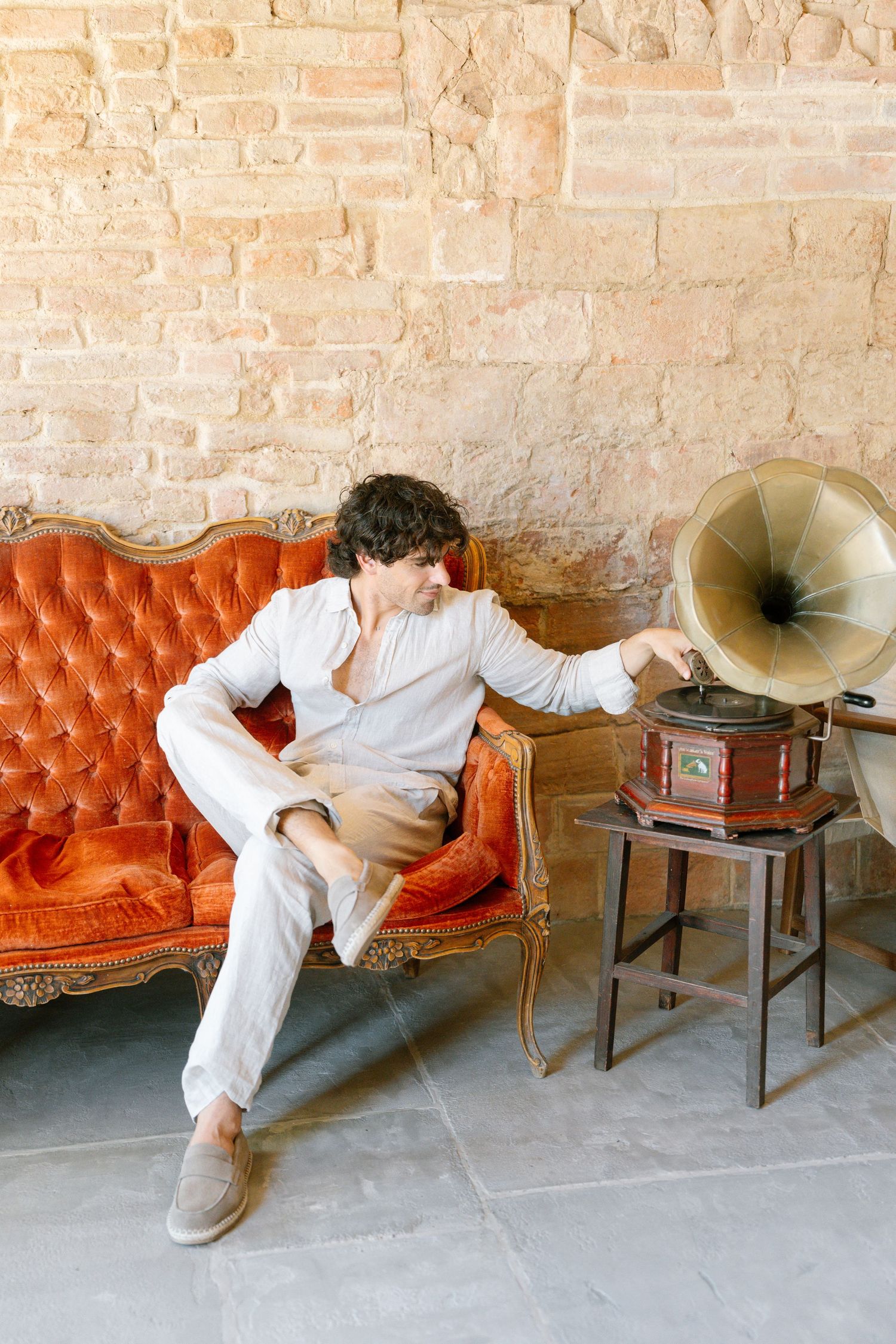 Person resting on a vintage orange leather couch next to an antique phonograph in a rustic brick room.