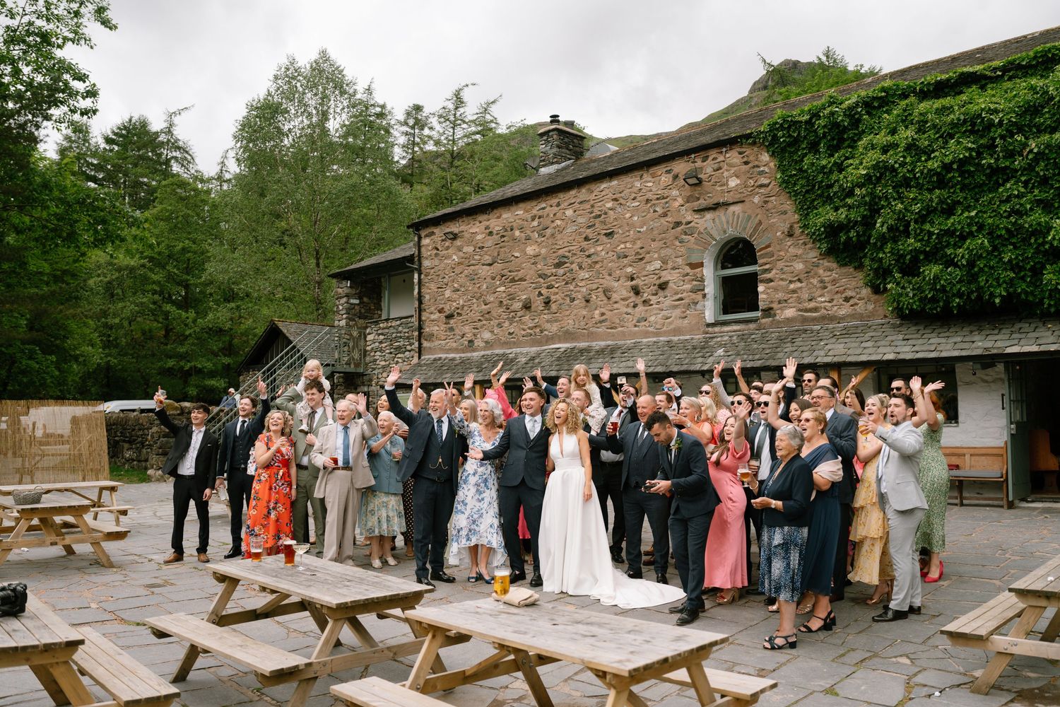 Wedding guests gather outside a rustic stone building during a celebration in the countryside.