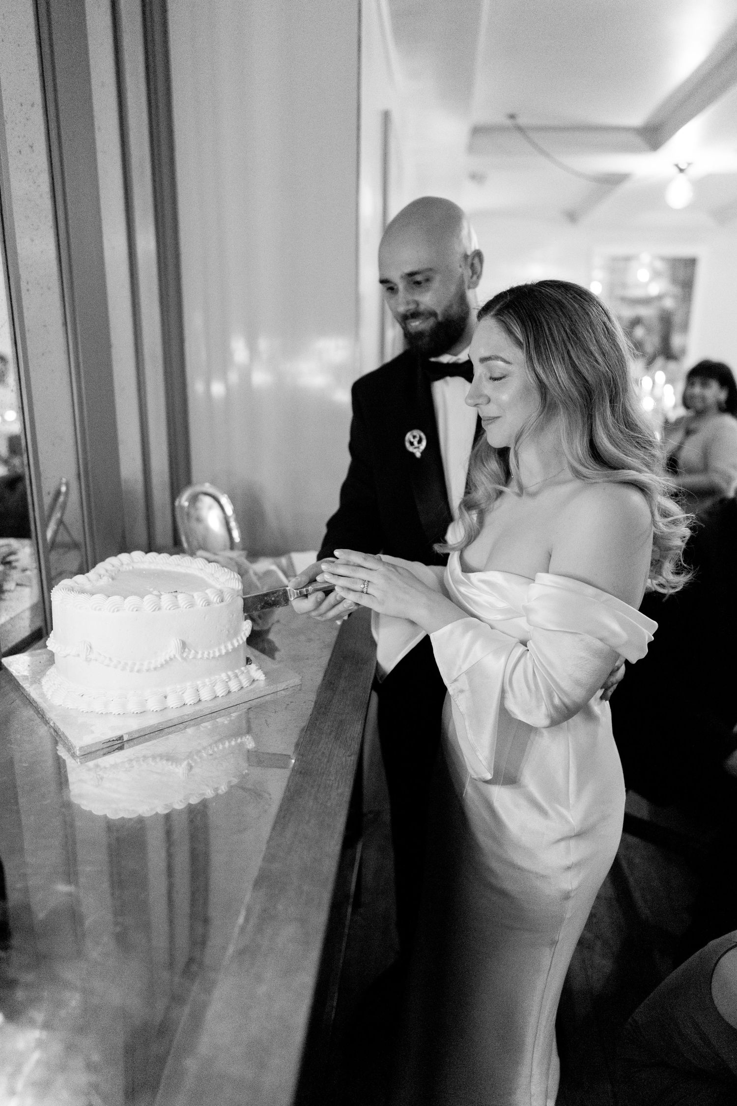 Couple cutting wedding cake together at reception in black and white.