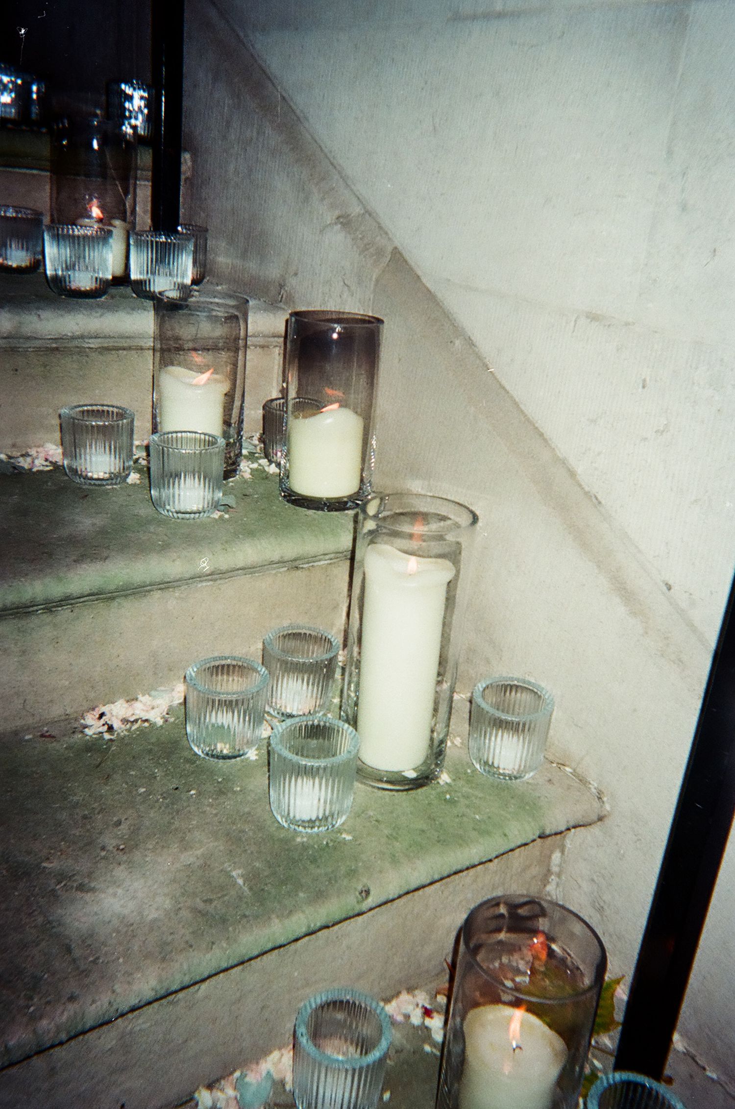 Row of glass votives and candles arranged on shelving in dim lighting.