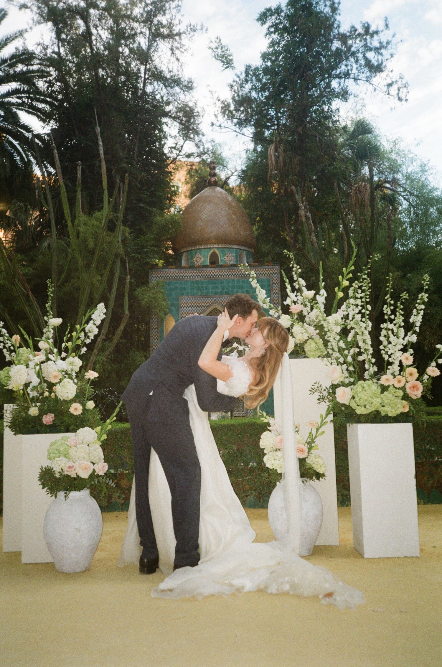 Romantic outdoor wedding scene with white floral arrangements on pedestals lining the ceremony space.