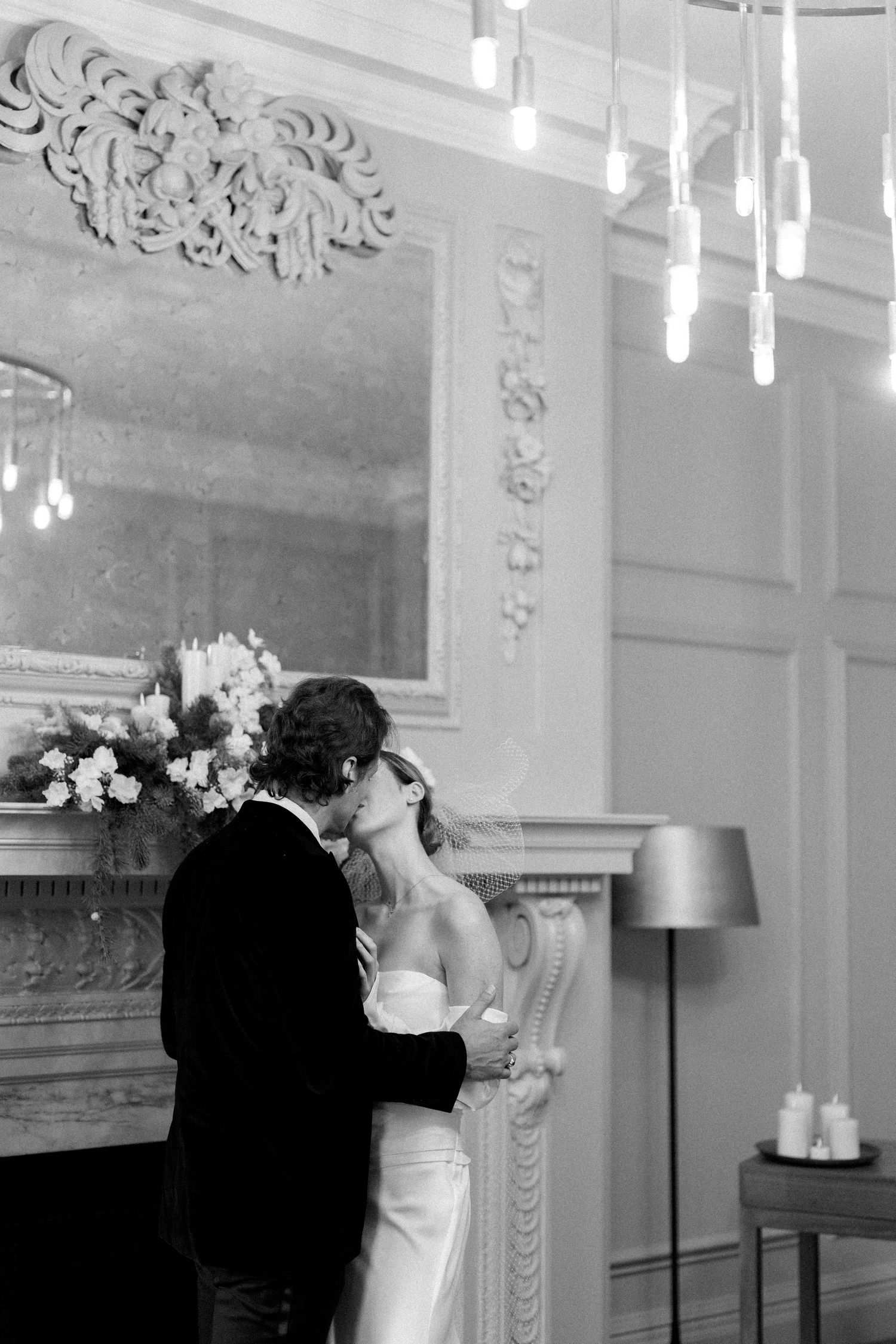 A romantic wedding moment captured under ornate white ceilings with hanging pendant lights.