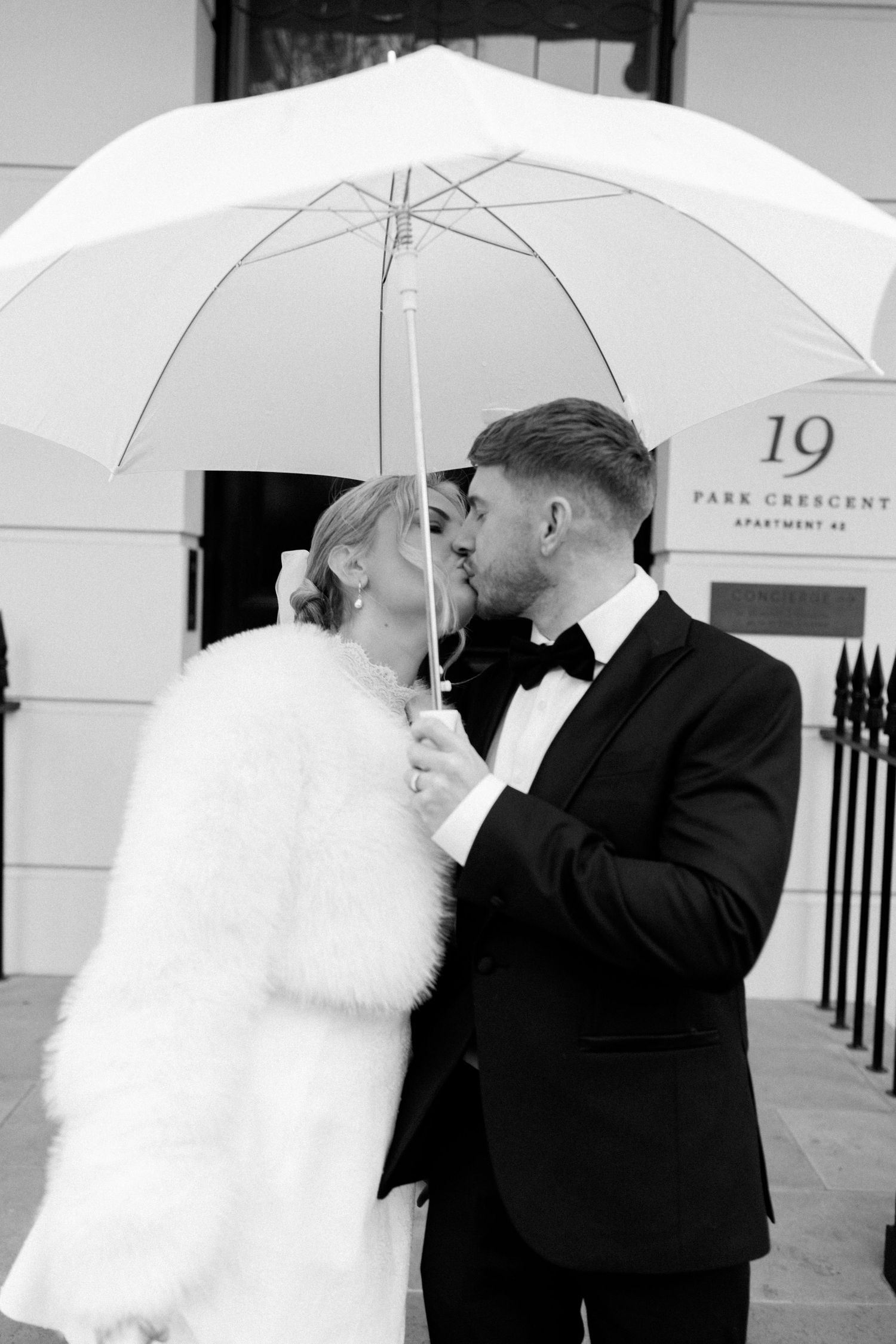 A romantic wedding photo series showing a couple with white umbrellas against a classic architectural backdrop.